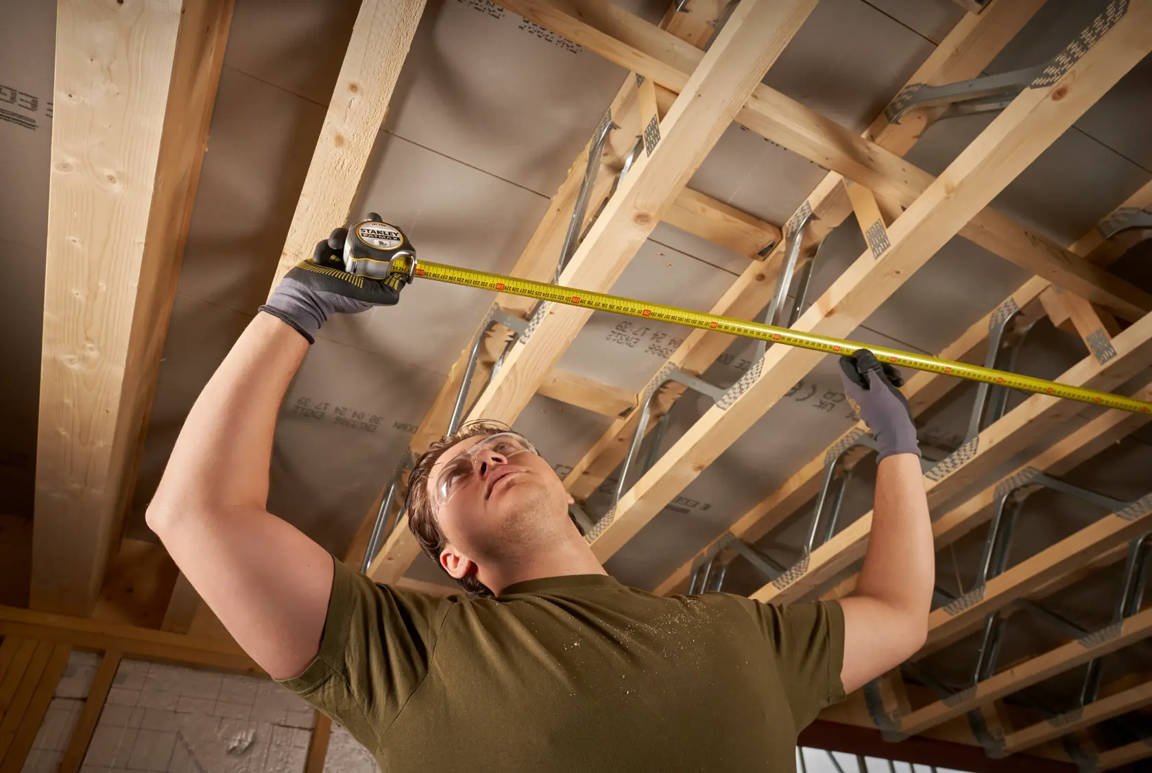 Metro a nastro STANLEY FMHT38214-0 utilizzato per misurare travi di legno sul soffitto in un interno in costruzione.
