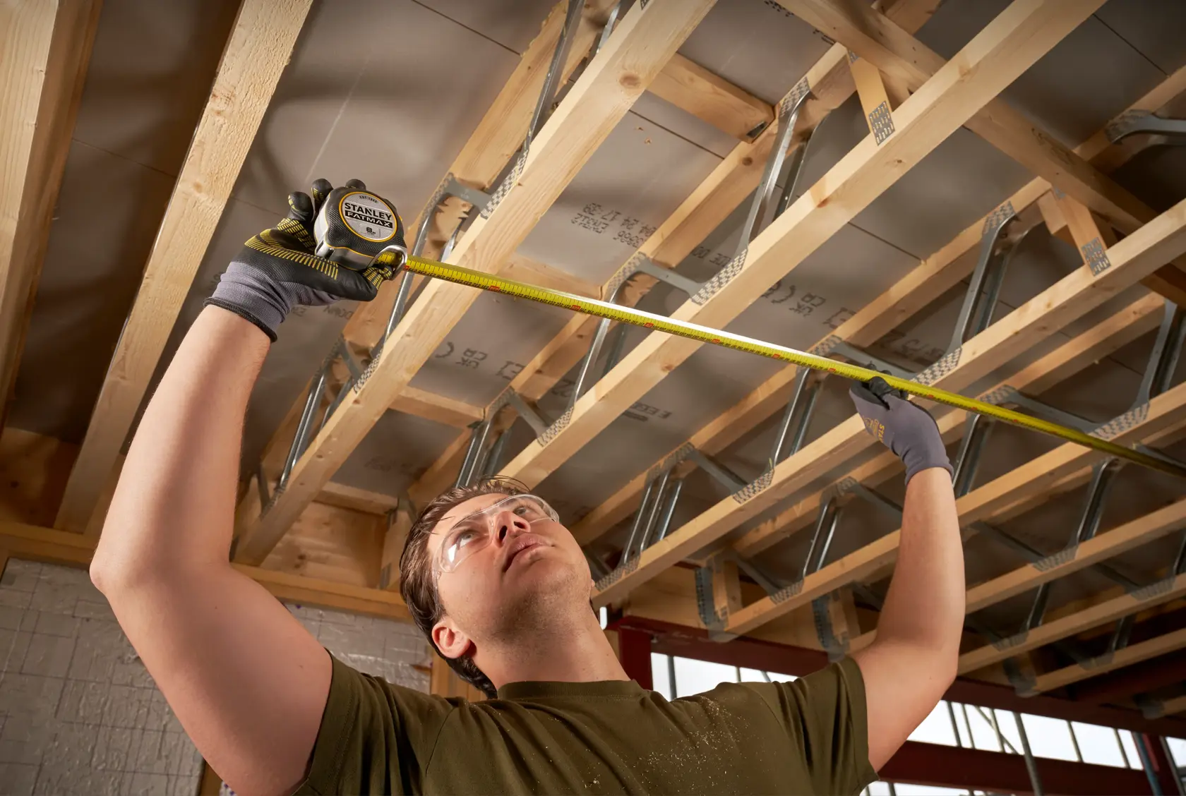 STANLEY FMHT38217-0 metro a nastro usato da una persona per misurare travi in legno sul soffitto in cantiere.