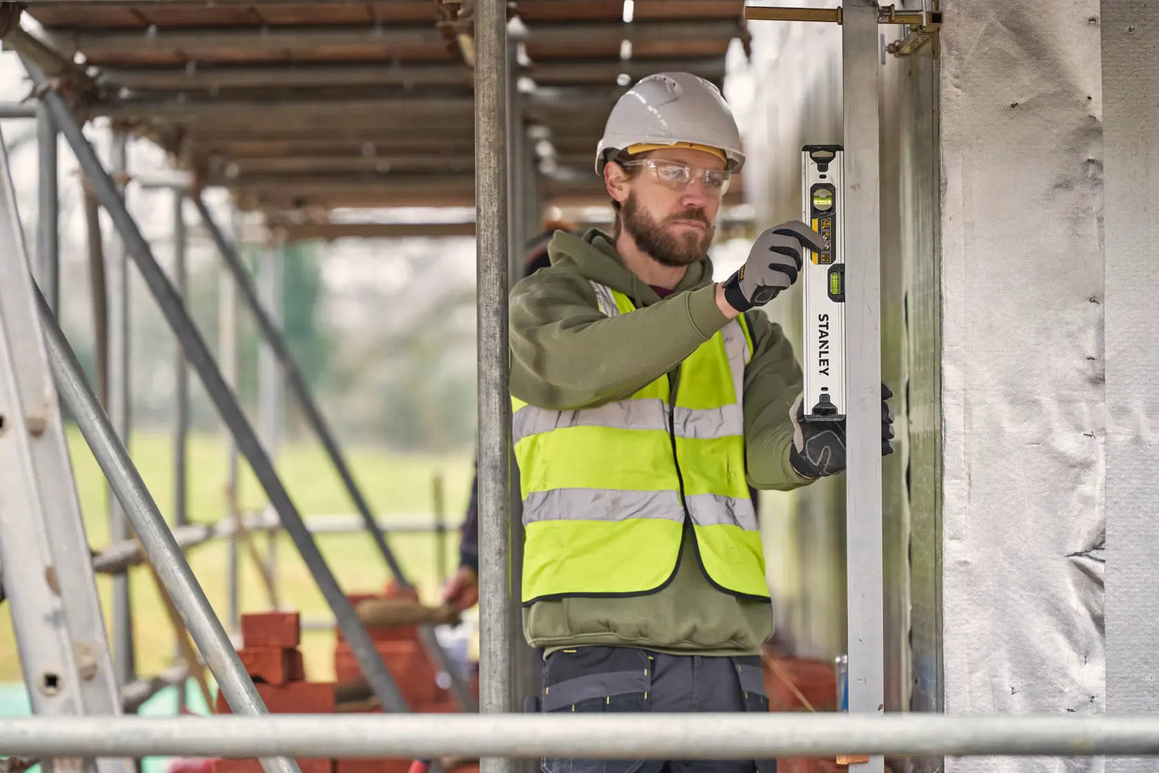 Foto di operaio che usa la livella STANLEY FMHT43671-1 in cantiere, con gilet ad alta visibilità e casco.