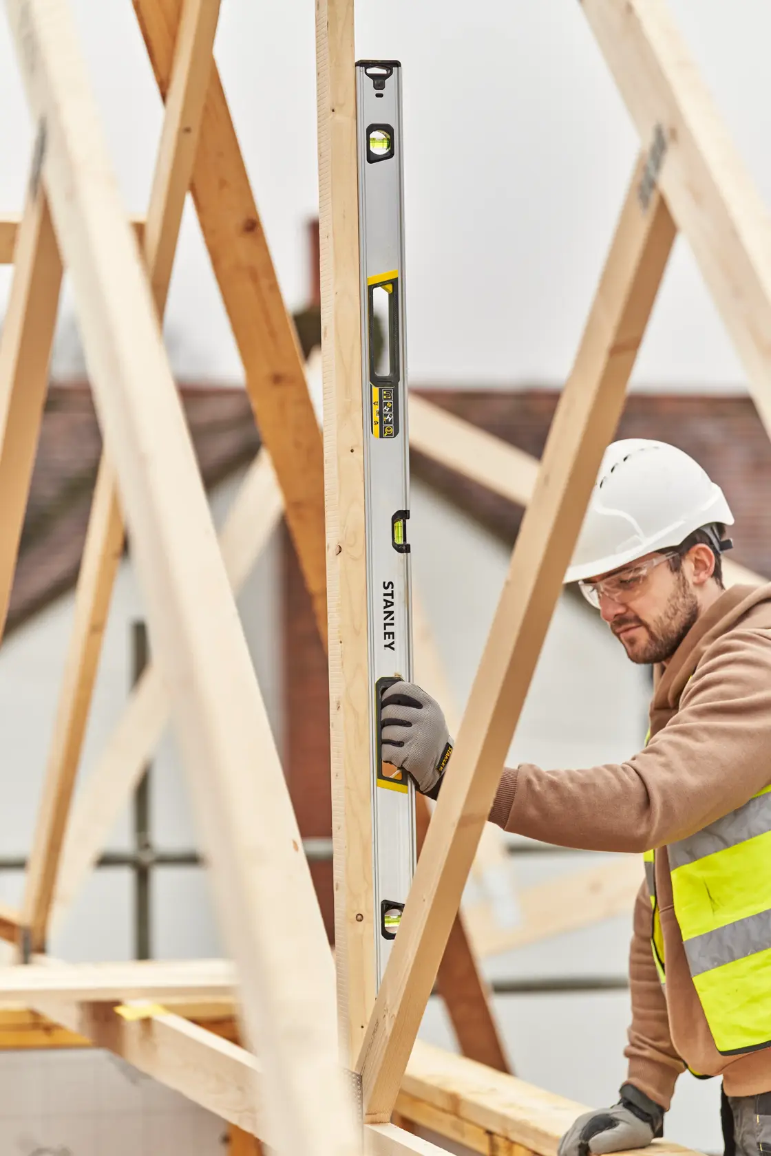 STANLEY FMHT43677 livella a bolla usata verticalmente da un operaio su travi di legno in cantiere.