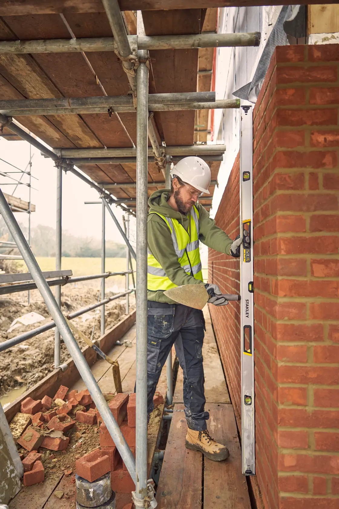 Livella STANLEY FMHT43678-1 utilizzata da un operaio per controllare l'allineamento verticale di un muro in mattoni in cantiere.