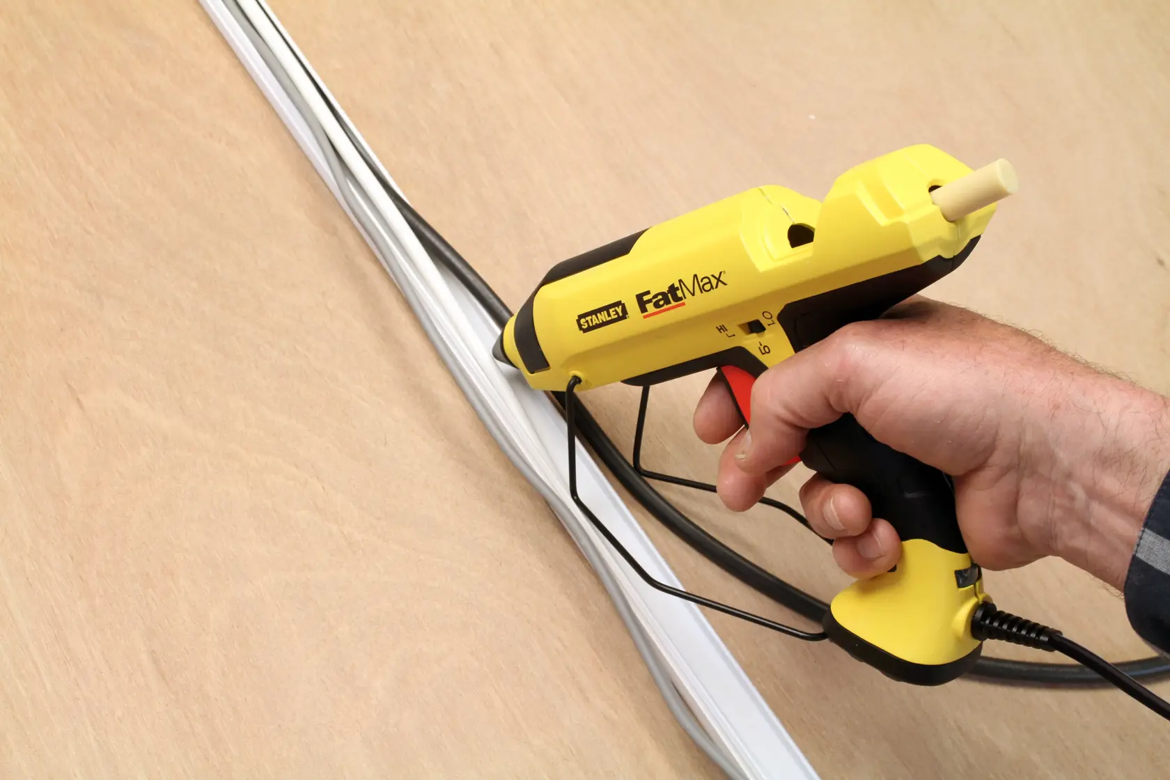 Stanley FMHT6-70418 pistola per colla gialla e nera in mano, adesivo su fili su superficie di legno.
