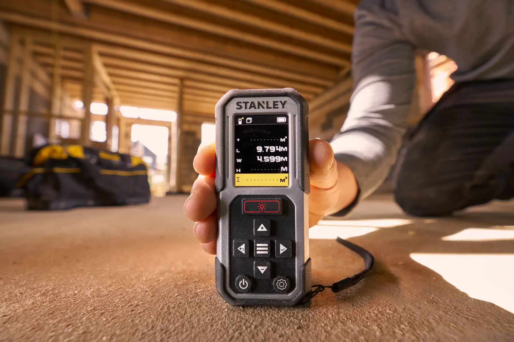 Fotografia del misuratore laser di distanza STANLEY FMHT77050-XJ tenuto in un cantiere, schermo visibile.