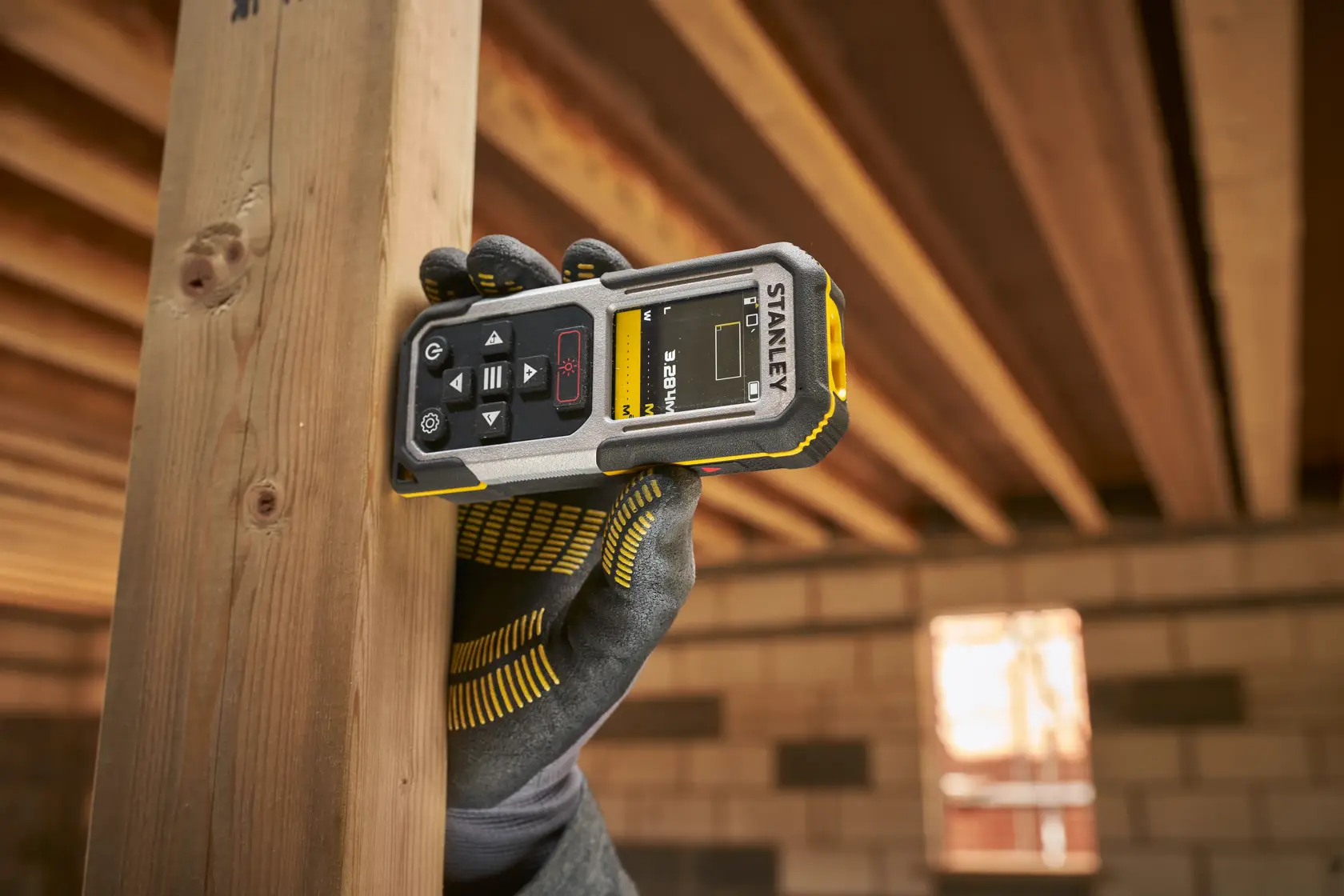 Foto del misuratore laser STANLEY FMHT77050-XJ in uso, con display e pulsanti visibili, tenuto da una mano guantata.