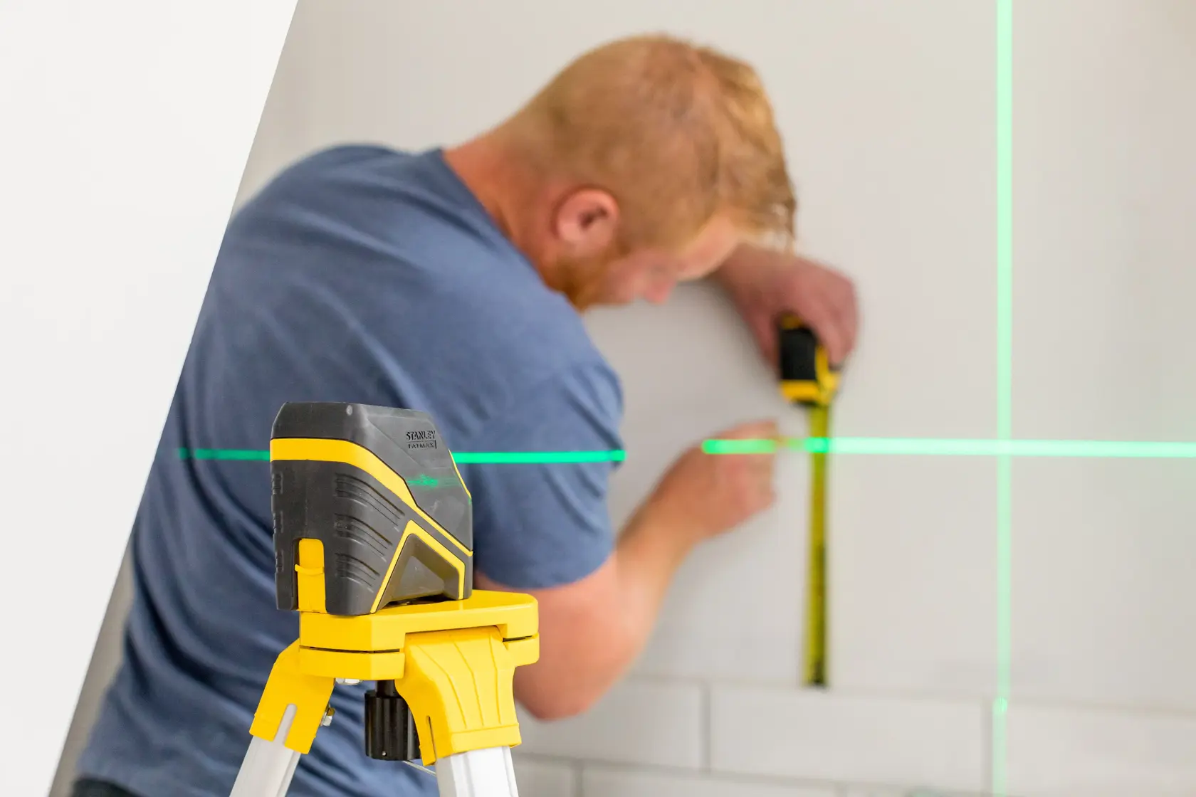 STANLEY FMHT77586-1 livello laser su treppiede con linee verdi, persona misura la parete.