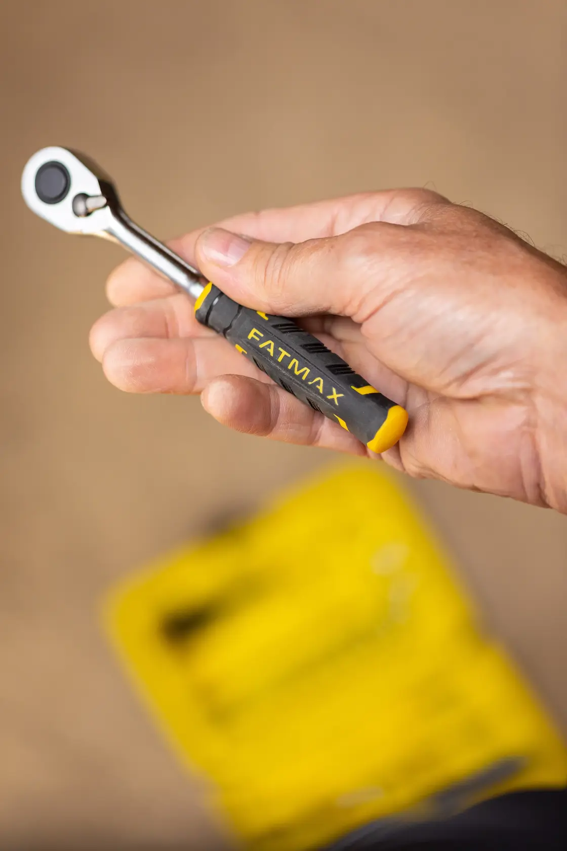 Mano che tiene la chiave a cricchetto compatta nera e gialla STANLEY FMMT82676-0, marchio FATMAX visibile.
