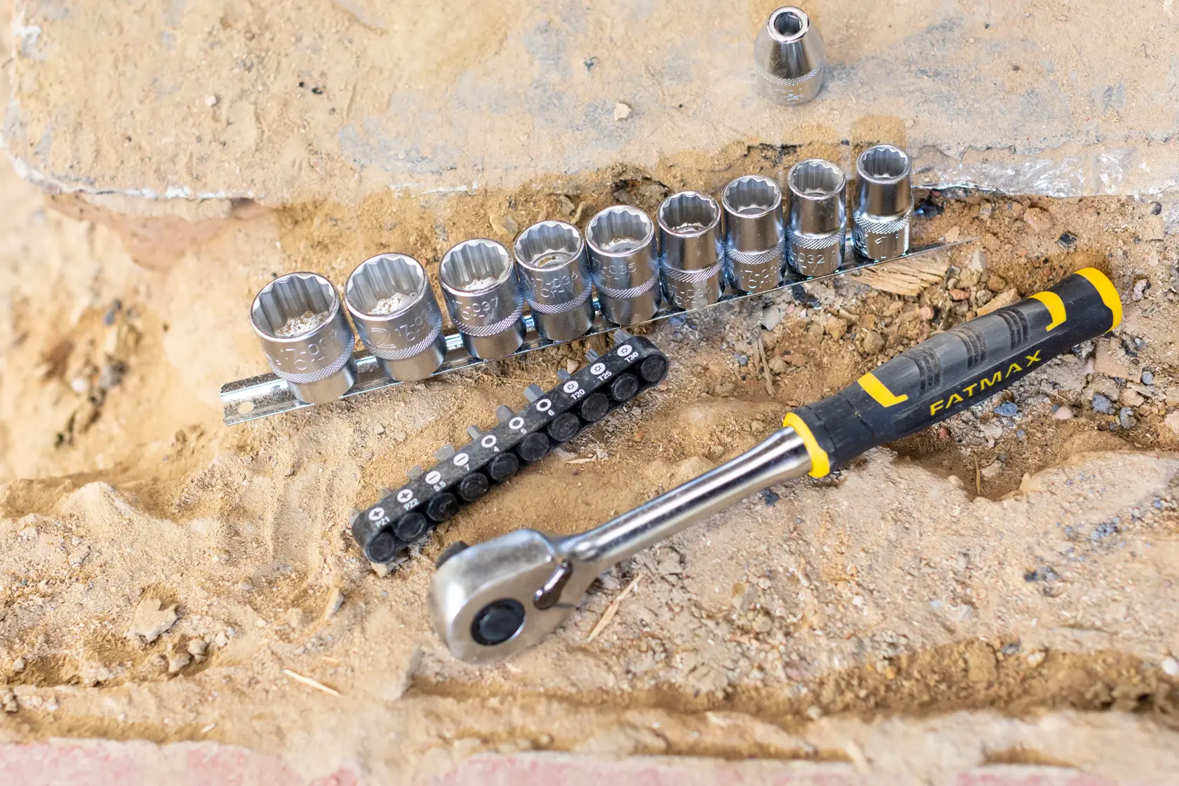 Set di chiavi a bussola STANLEY FMMT82681-0 con cricchetto e bussole su superficie sabbiosa, marchio FatMax visibile.