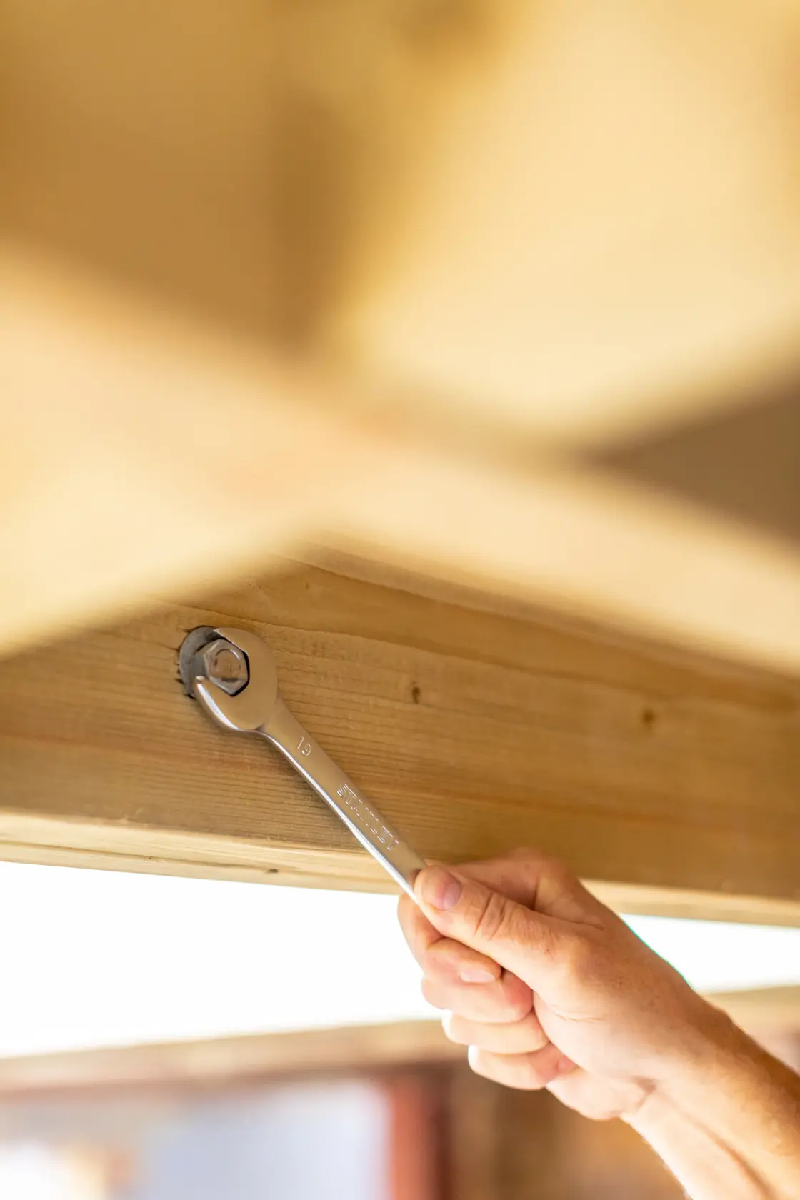 Chiave a cricchetto STANLEY FMMT82845-0 che stringe un bullone su trave in legno, mano che tiene l'attrezzo.
