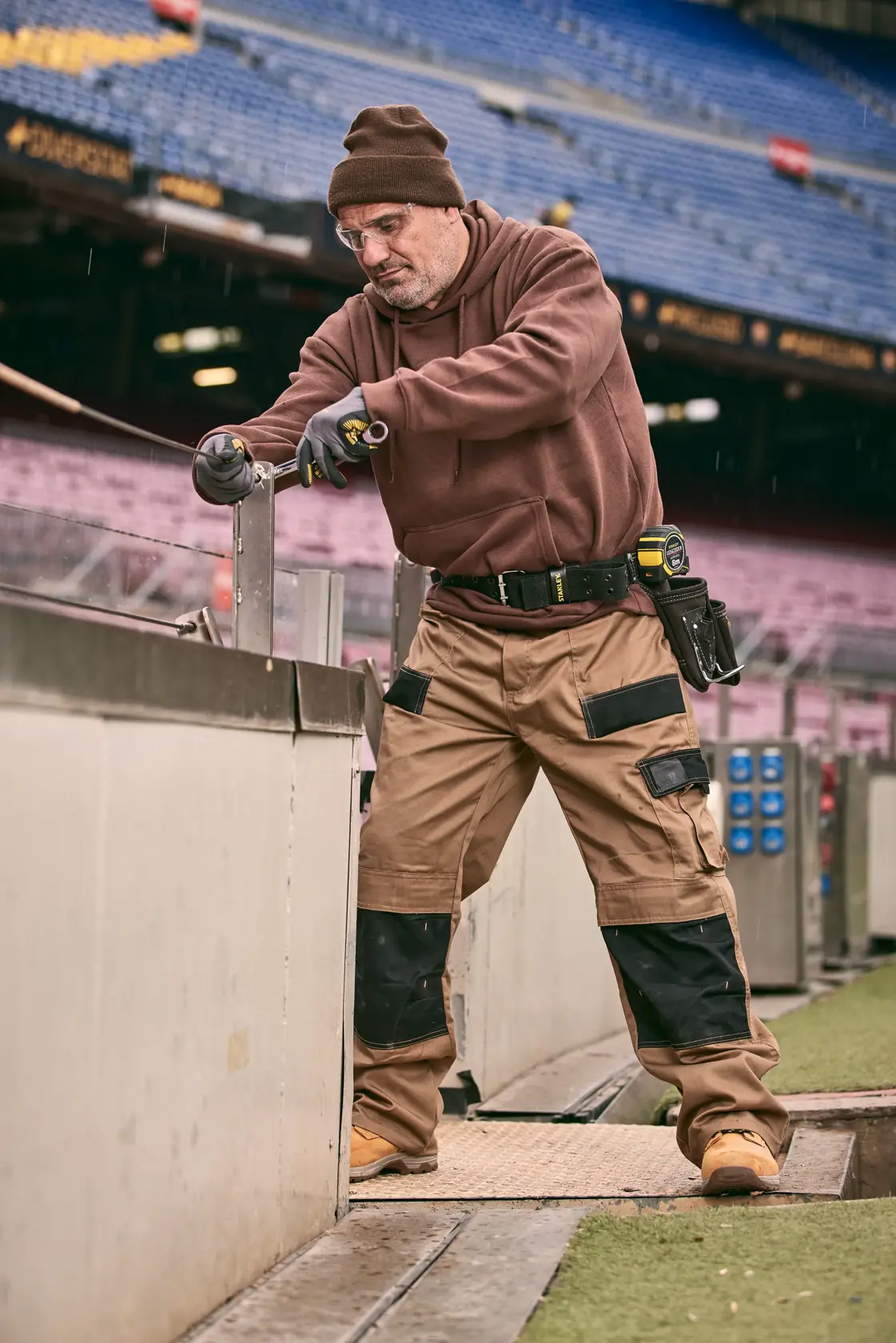 STANLEY FMMT82848-0 professionista con utensile, cintura portautensili e pantaloni da lavoro presso cantiere stadio.