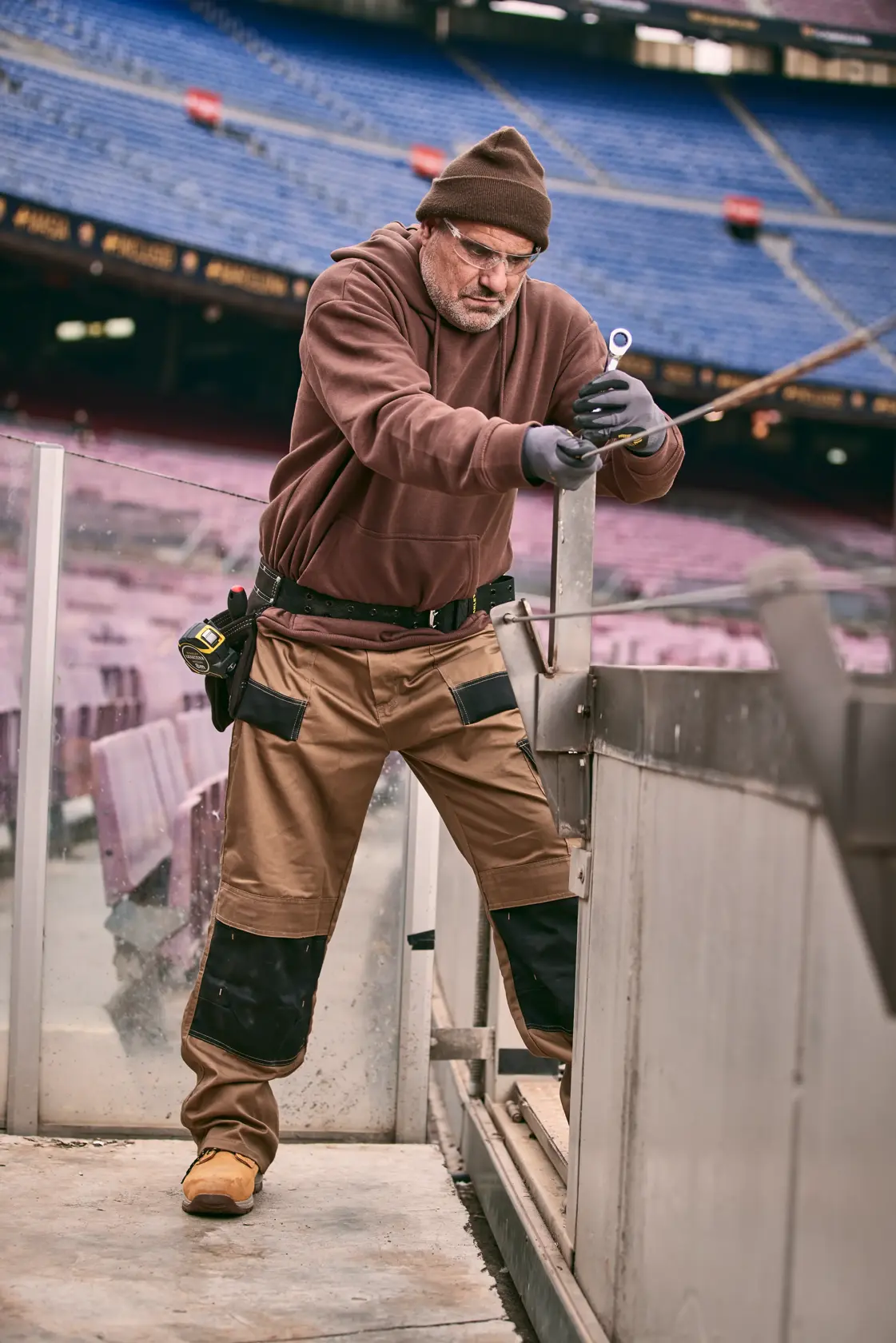 STANLEY FMMT82848-0 fotografia di un operaio in abbigliamento da lavoro marrone con utensile manuale in uno stadio vuoto.
