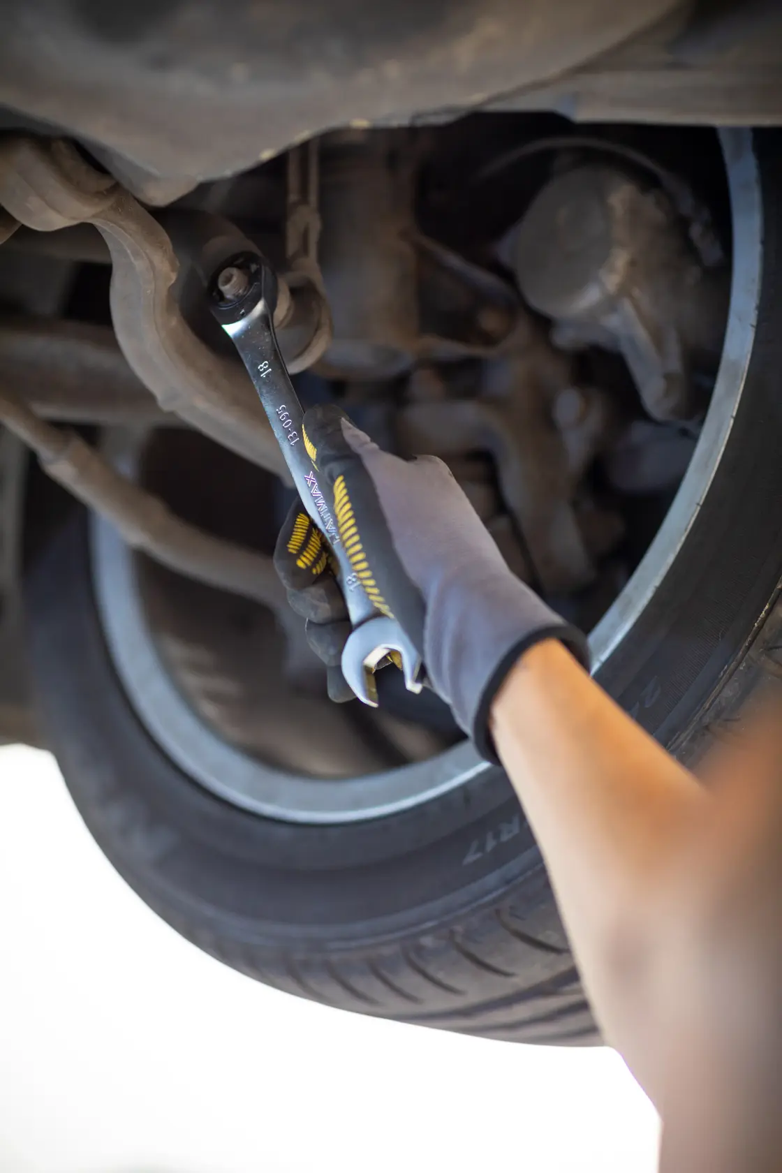 Chiave combinata STANLEY FMMT82849-0 usata su sospensione auto, primo piano con mano guantata e pneumatico.
