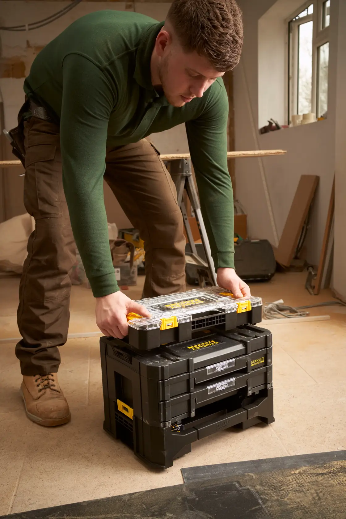 STANLEY FMMT98103-1 set di cassette degli attrezzi modulari nere con dettagli gialli in officina, persona che impila un organizer sopra.