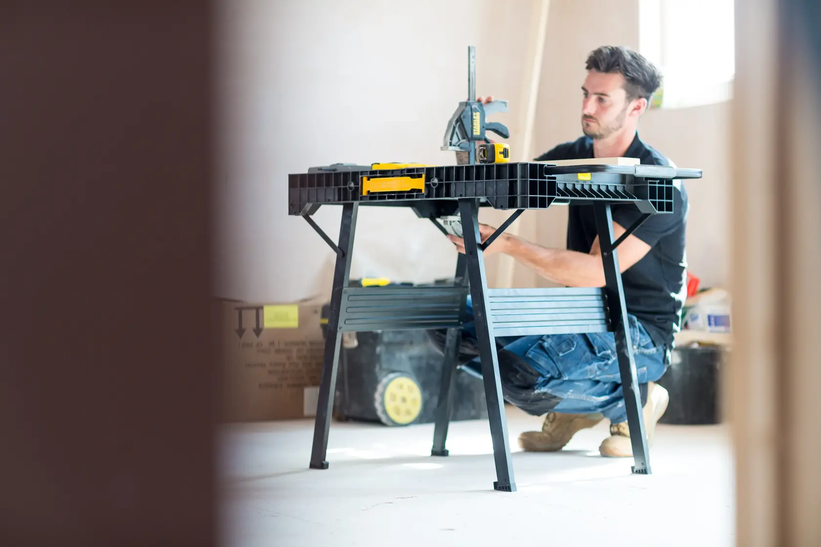 Foto del banco da lavoro STANLEY FMST1-75672 in uso in cantiere, persona inginocchiata accanto al tavolo pieghevole nero.