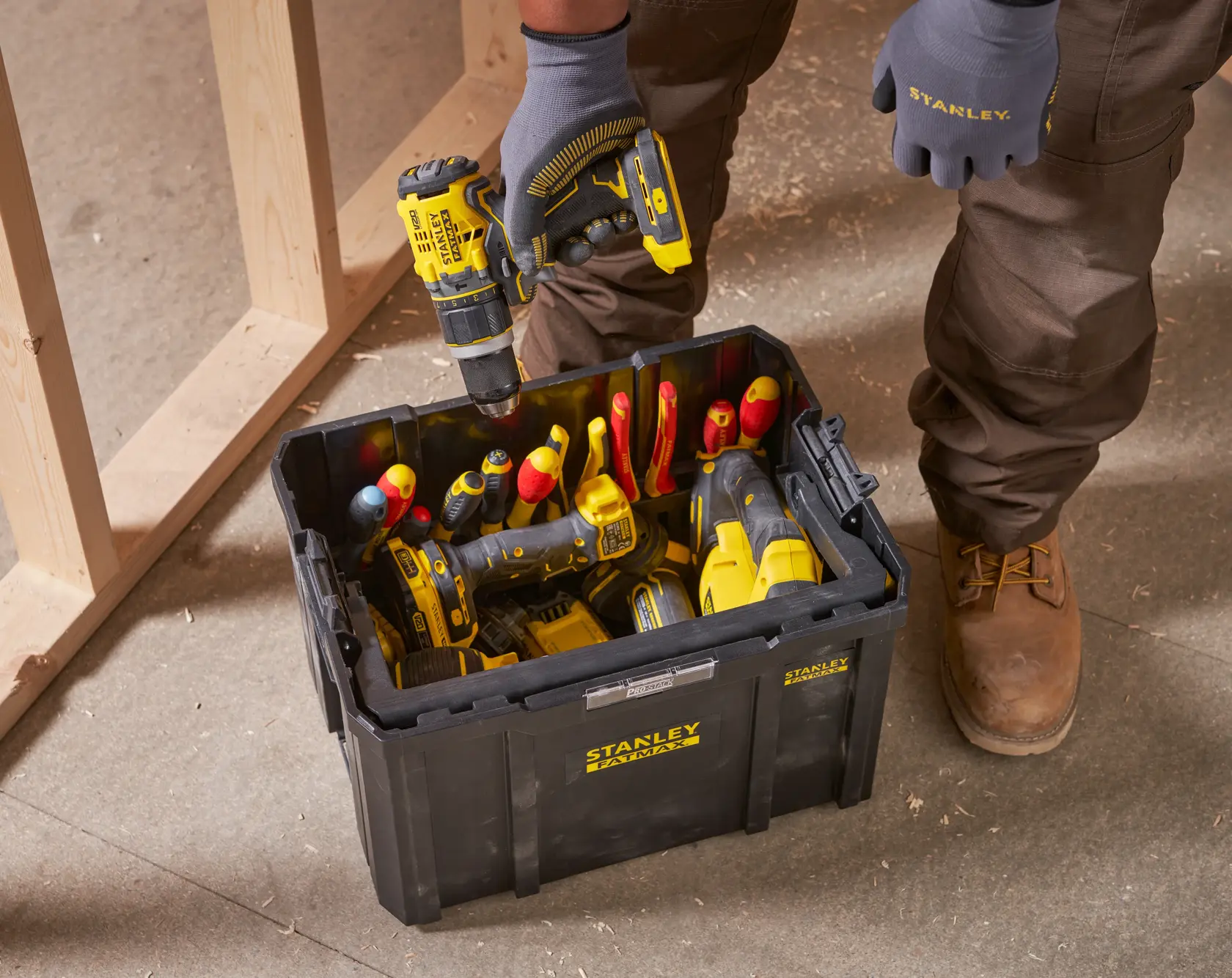 STANLEY FMST1-75794 cassetta degli attrezzi nera su pavimento del cantiere, piena di utensili manuali e elettrici, persona con trapano.
