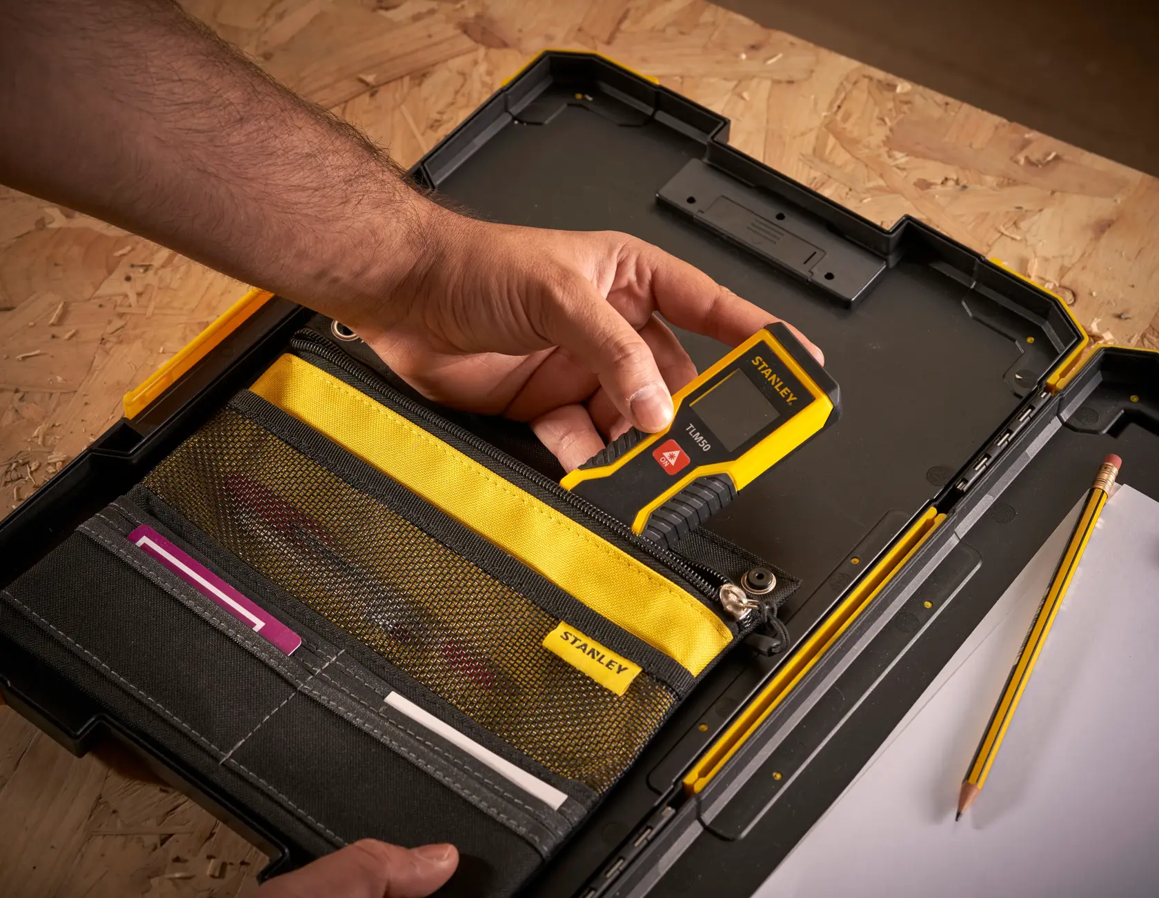 Foto della valigetta porta attrezzi STANLEY FMST82721-1 con organizer giallo e nero, mano che tiene uno strumento di misura digitale.