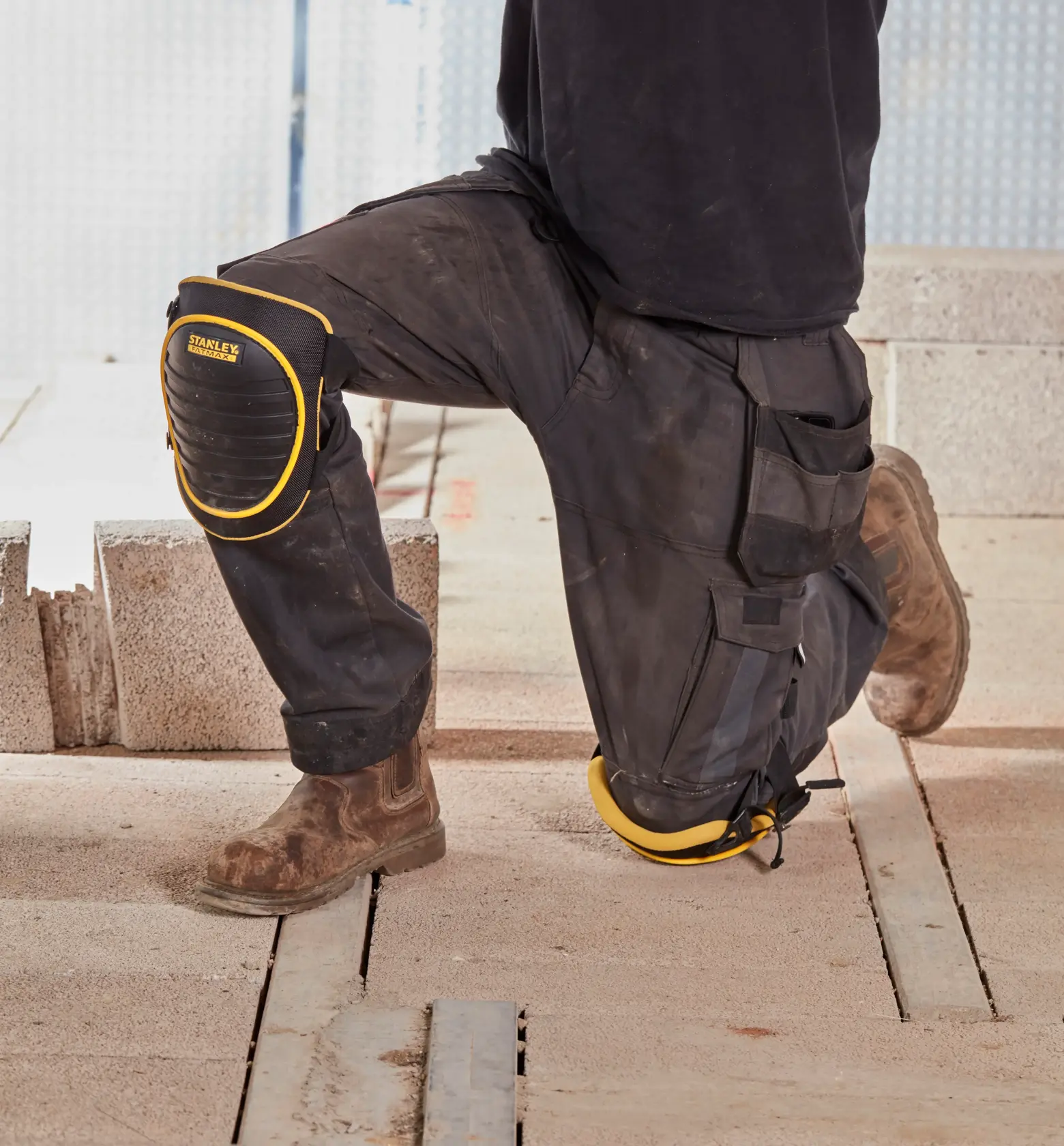 Ginocchiere STANLEY FMST82961-1 nere con bordo giallo indossate su pantaloni da lavoro in un cantiere.