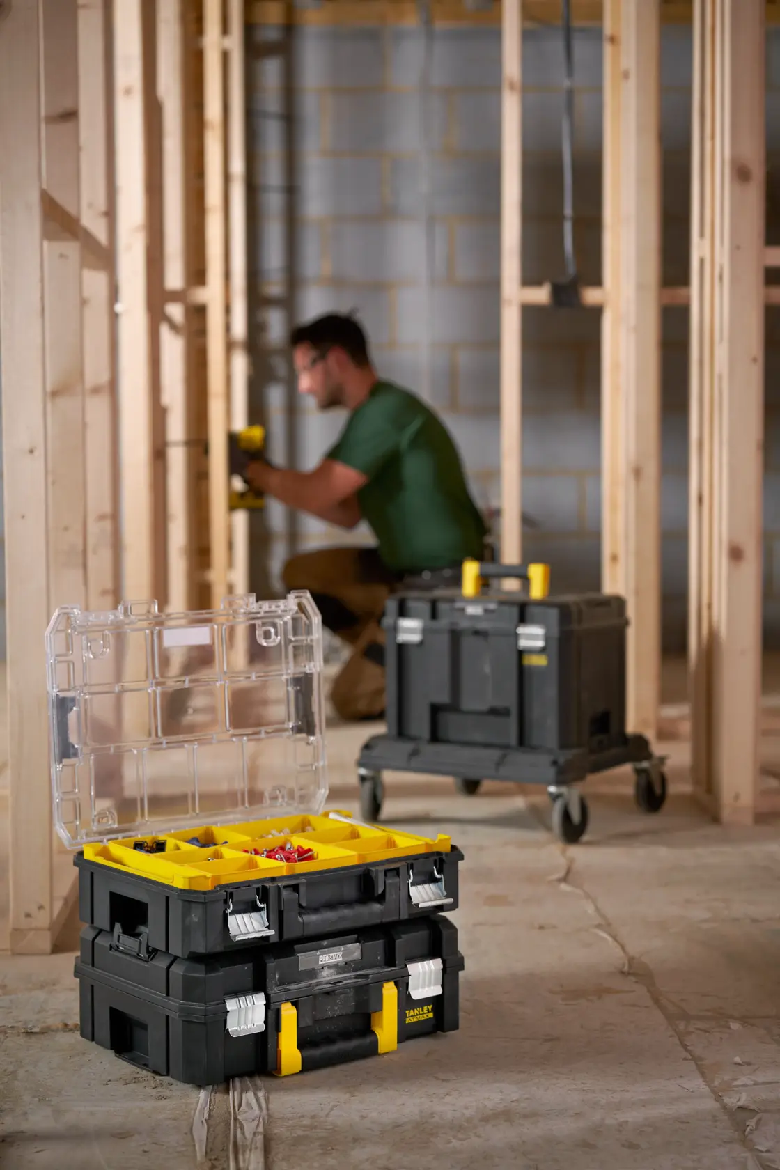 STANLEY FMST82967-1 organizer per attrezzi nero e giallo con coperchio trasparente aperto, impilato su un'altra scatola in un cantiere.