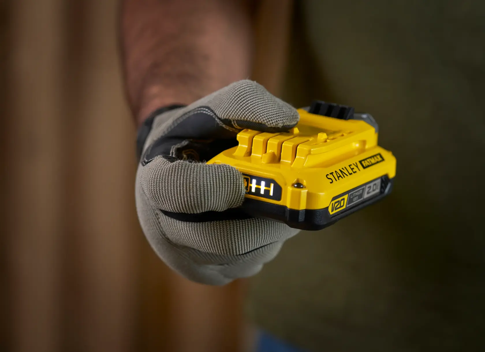 Fotografia della batteria V20 gialla STANLEY SFMCB12D2 tenuta in mano con guanto, primo piano prodotto.