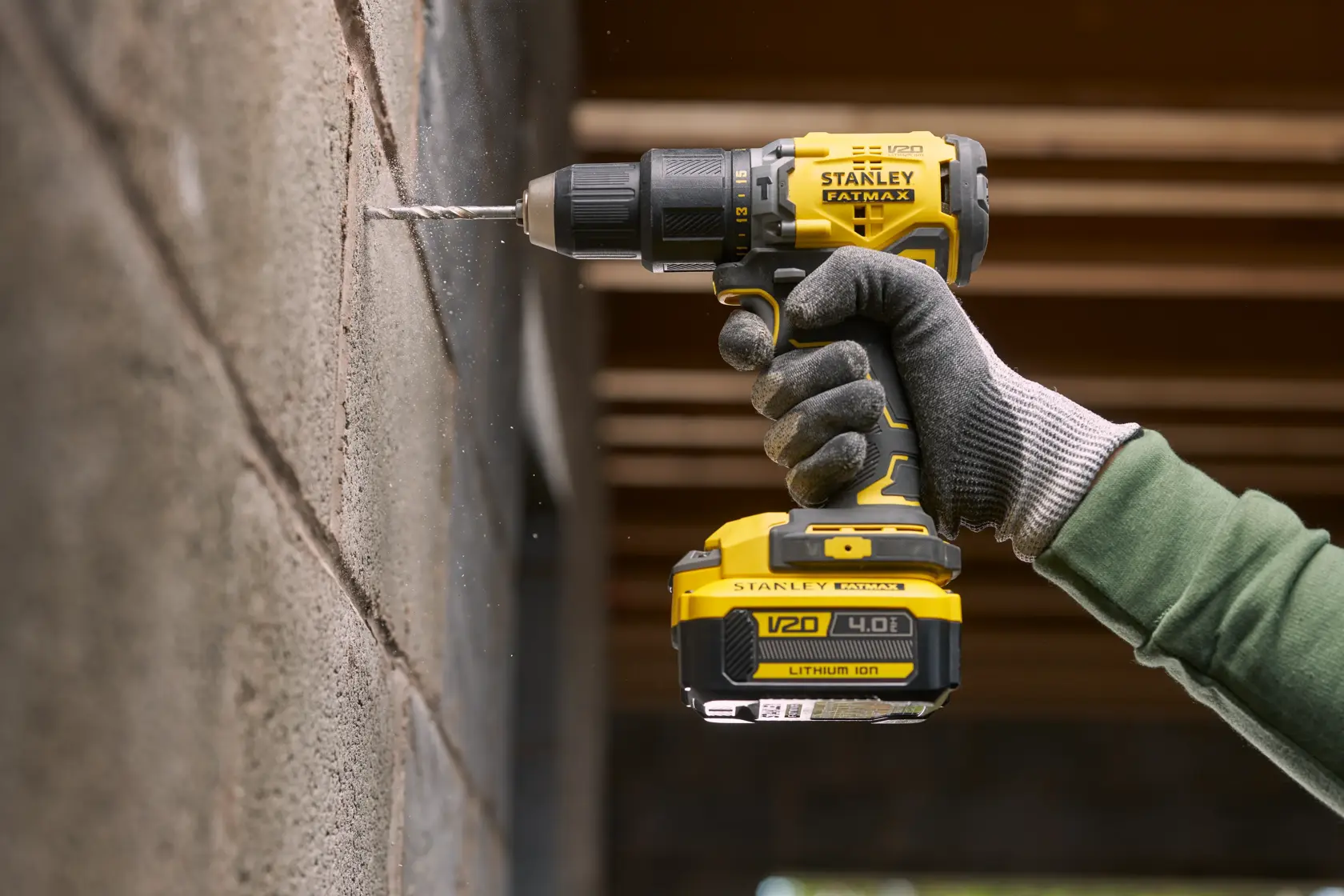 Trapano a batteria STANLEY SFMCB14M1 in uso, foratura su muro in cemento, vista ravvicinata dello strumento e mano con guanto.