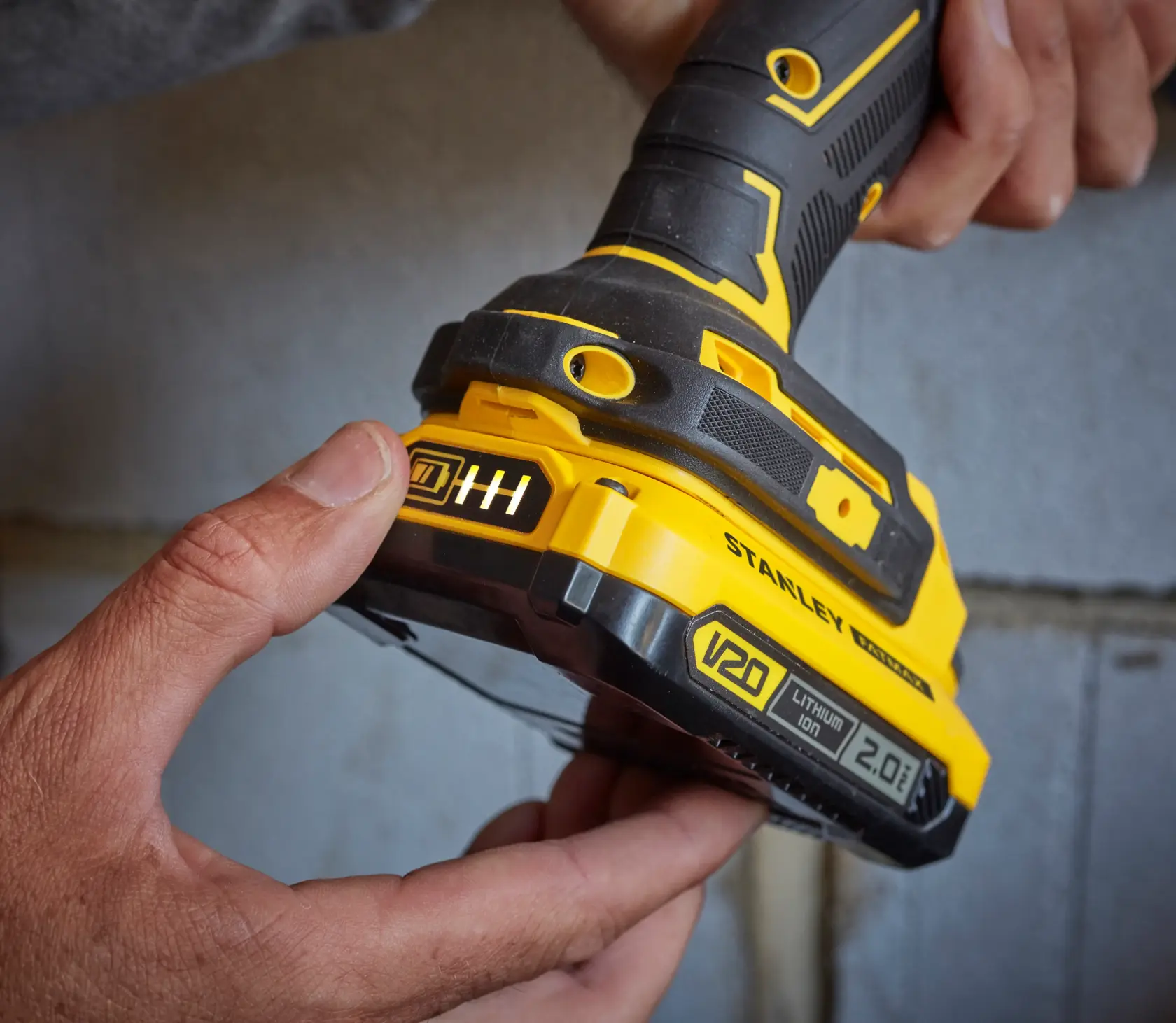 Fotografia della batteria STANLEY SFMCB202 V20 Lithium Ion 2.0Ah collegata a utensile elettrico giallo e nero.