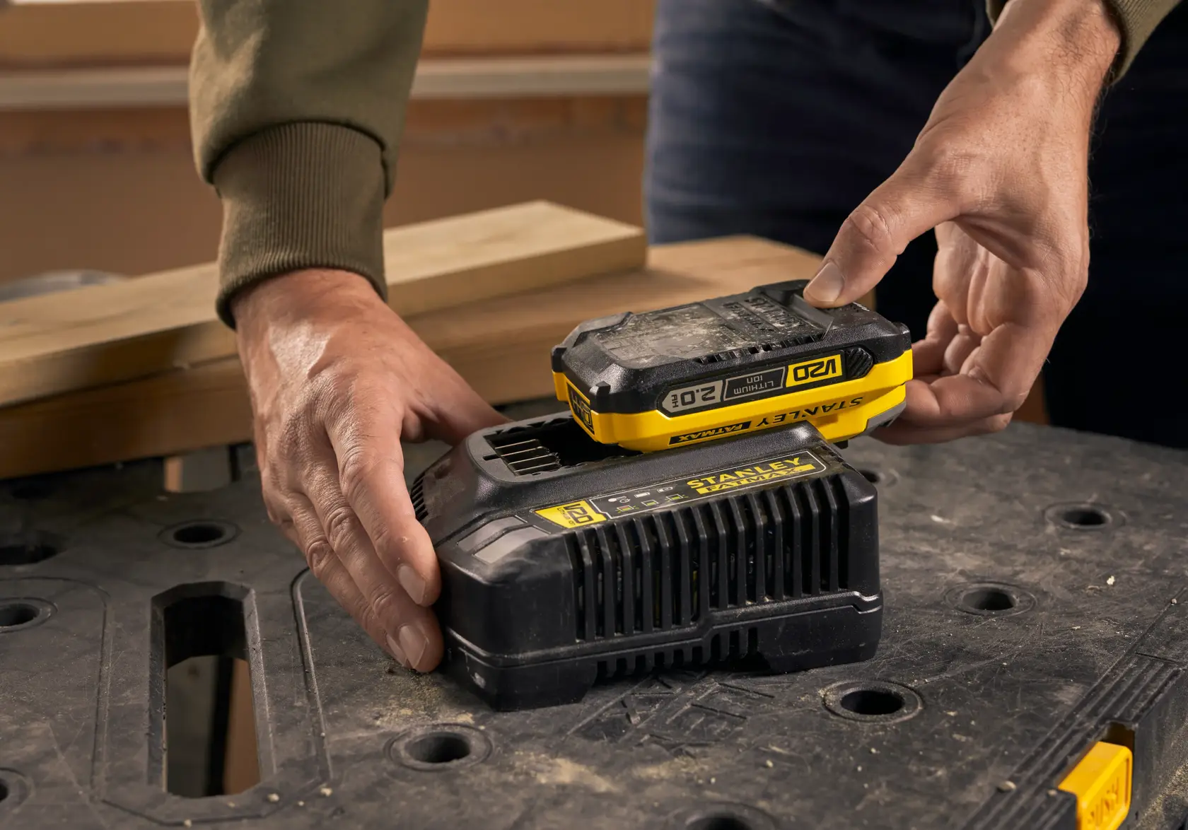 Batteria STANLEY SFMCB202 posizionata su caricatore nero, primo piano con banco da lavoro sullo sfondo.