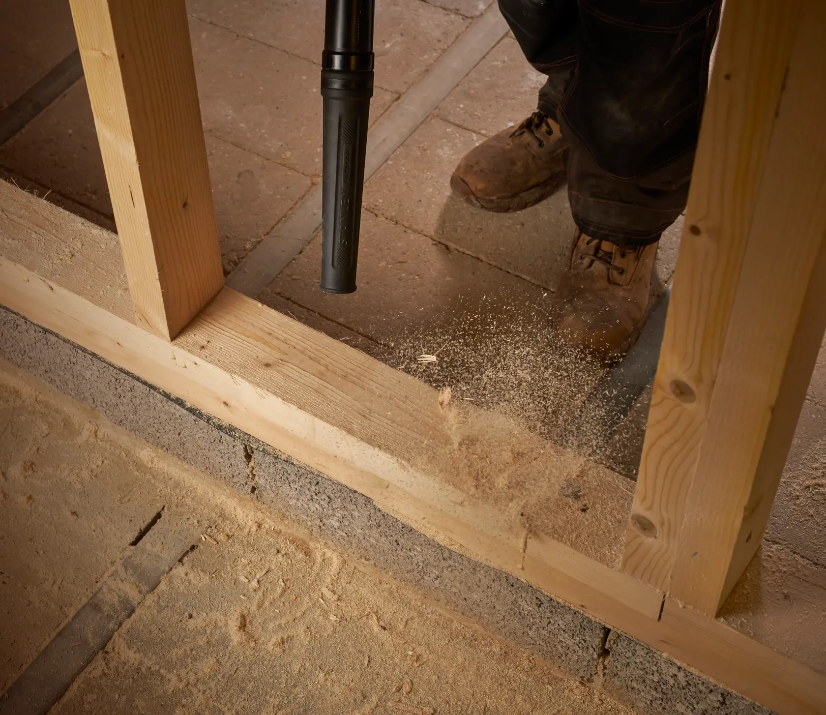 STANLEY SFMCBL01B soffiatore che pulisce segatura sul pavimento in cantiere, primo piano di ugello e scarpe da lavoro.