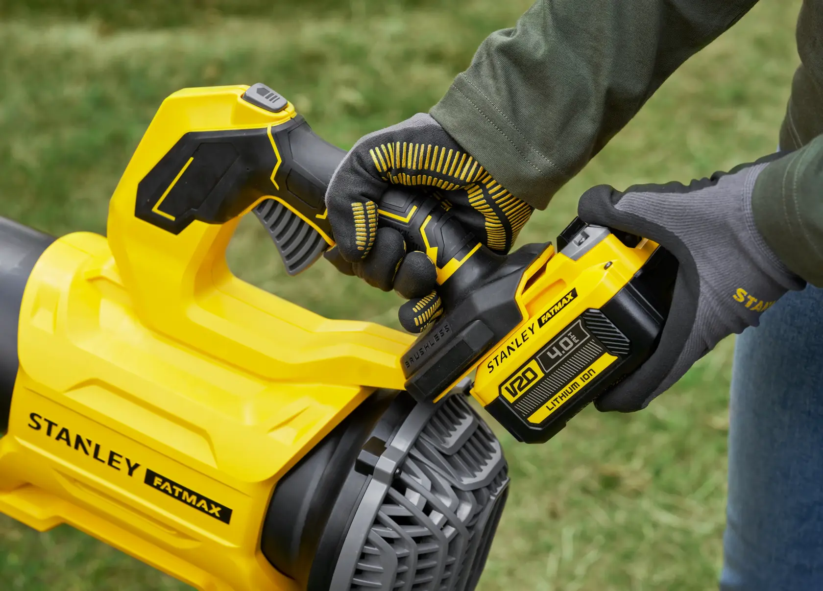 STANLEY SFMCBL730B soffiatore di foglie, primo piano su manico e batteria gialli, uso esterno, persona con guanti.
