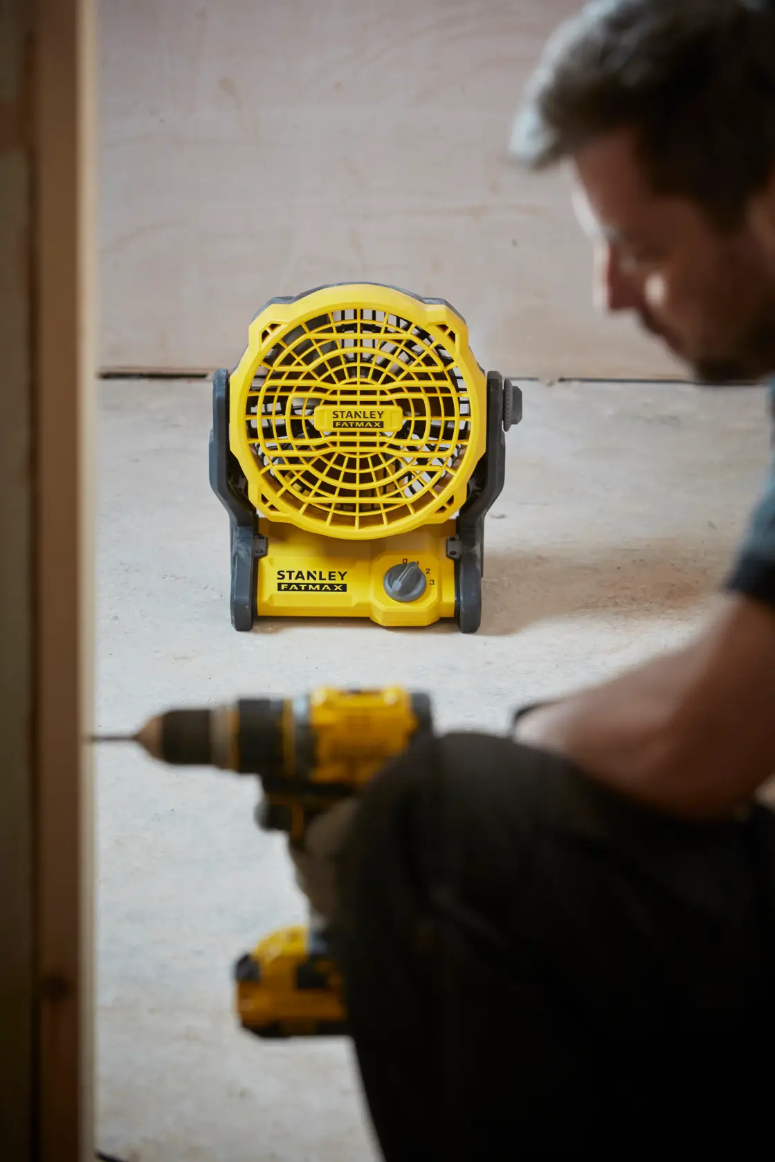 Foto del ventilatore portatile giallo STANLEY SFMCE001B sul pavimento con utensile da costruzione in primo piano.