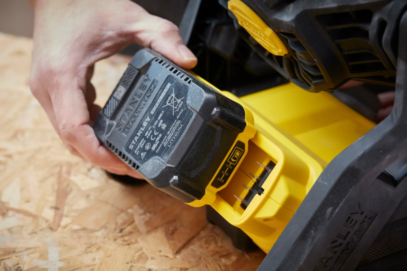 Fotografia della batteria STANLEY SFMCE001B inserita in un utensile elettrico giallo su superficie di legno.