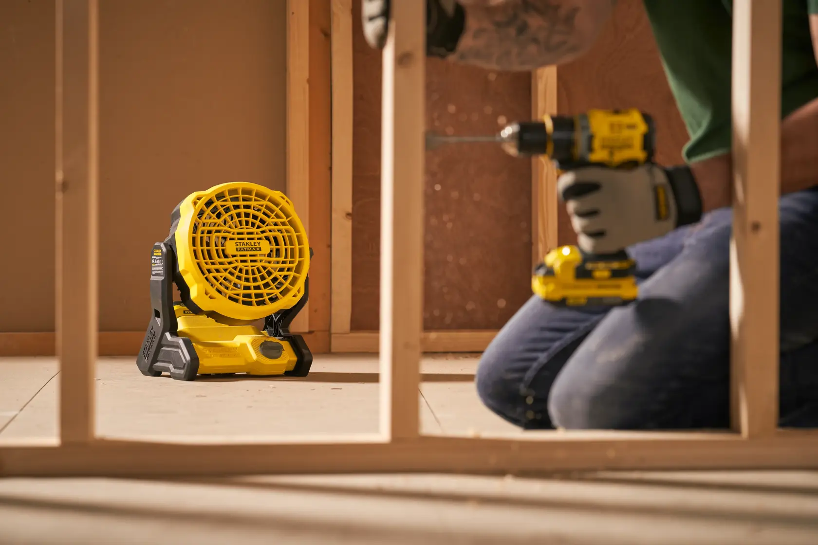 Ventilatore portatile da cantiere Stanley SFMCE001B sul pavimento in un'area di costruzione, operaio usa trapano vicino.