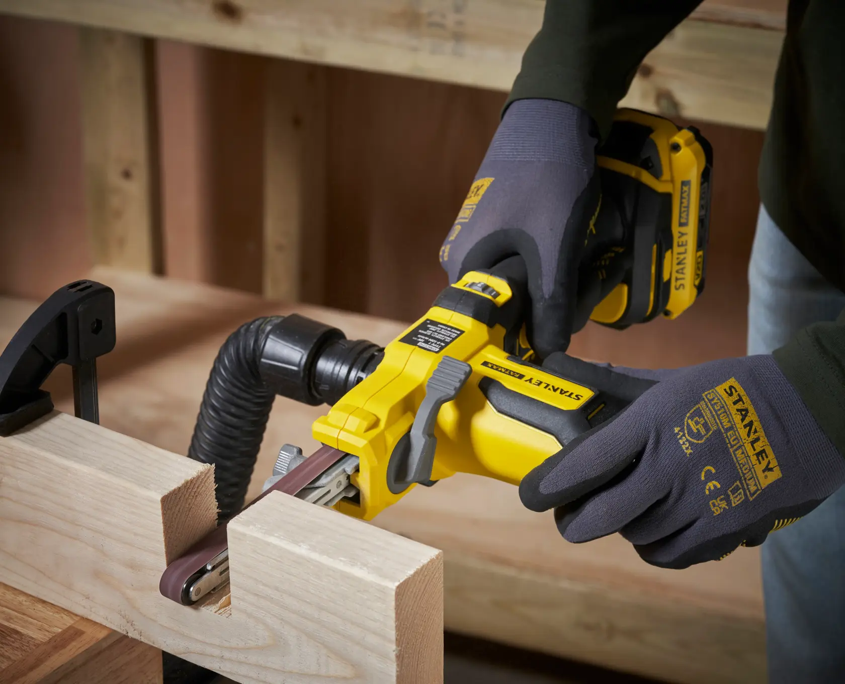 Foto della levigatrice a nastro senza fili STANLEY SFMCE210B in uso su una superficie in legno, operatore con guanti.