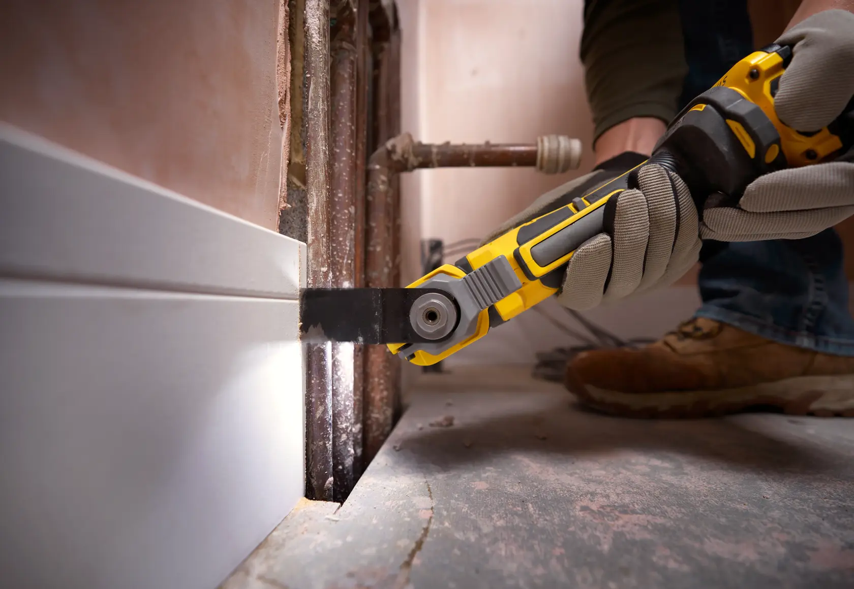 STANLEY SFMCE510B utensile multifunzione oscillante taglia battiscopa vicino a tubi, primo piano durante la ristrutturazione.
