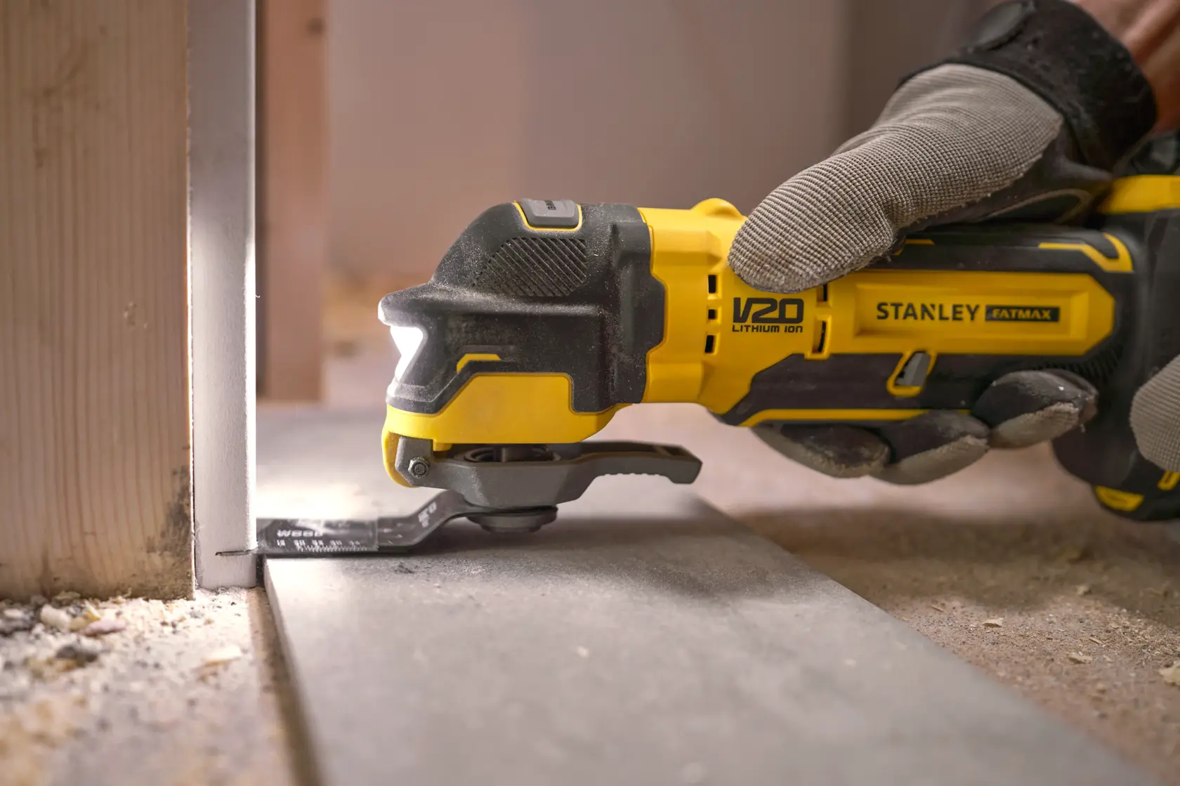 Stanley SFMCE510M2K utensile multifunzione oscillante taglia pannello pavimento, primo piano con guanto, cantiere.