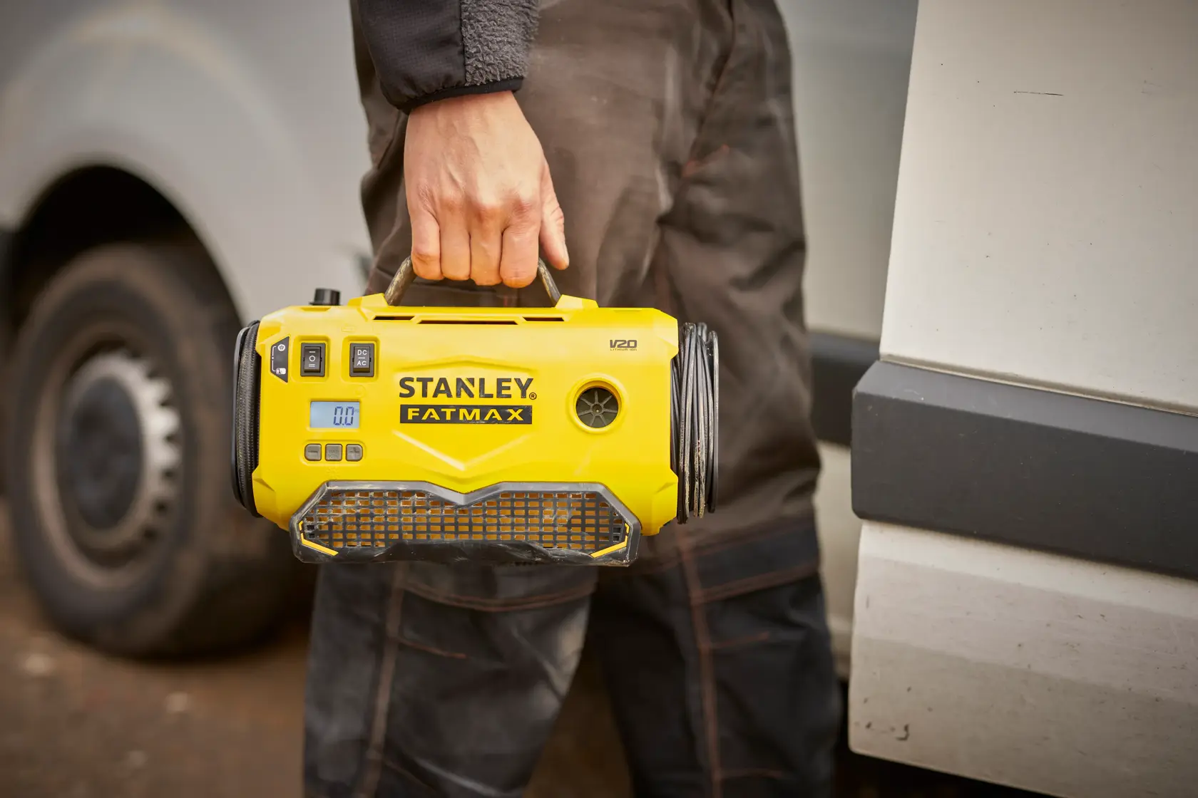 Stanley SFMCE520B gonfiatore portatile giallo tenuto dal manico, all'aperto vicino a un veicolo.
