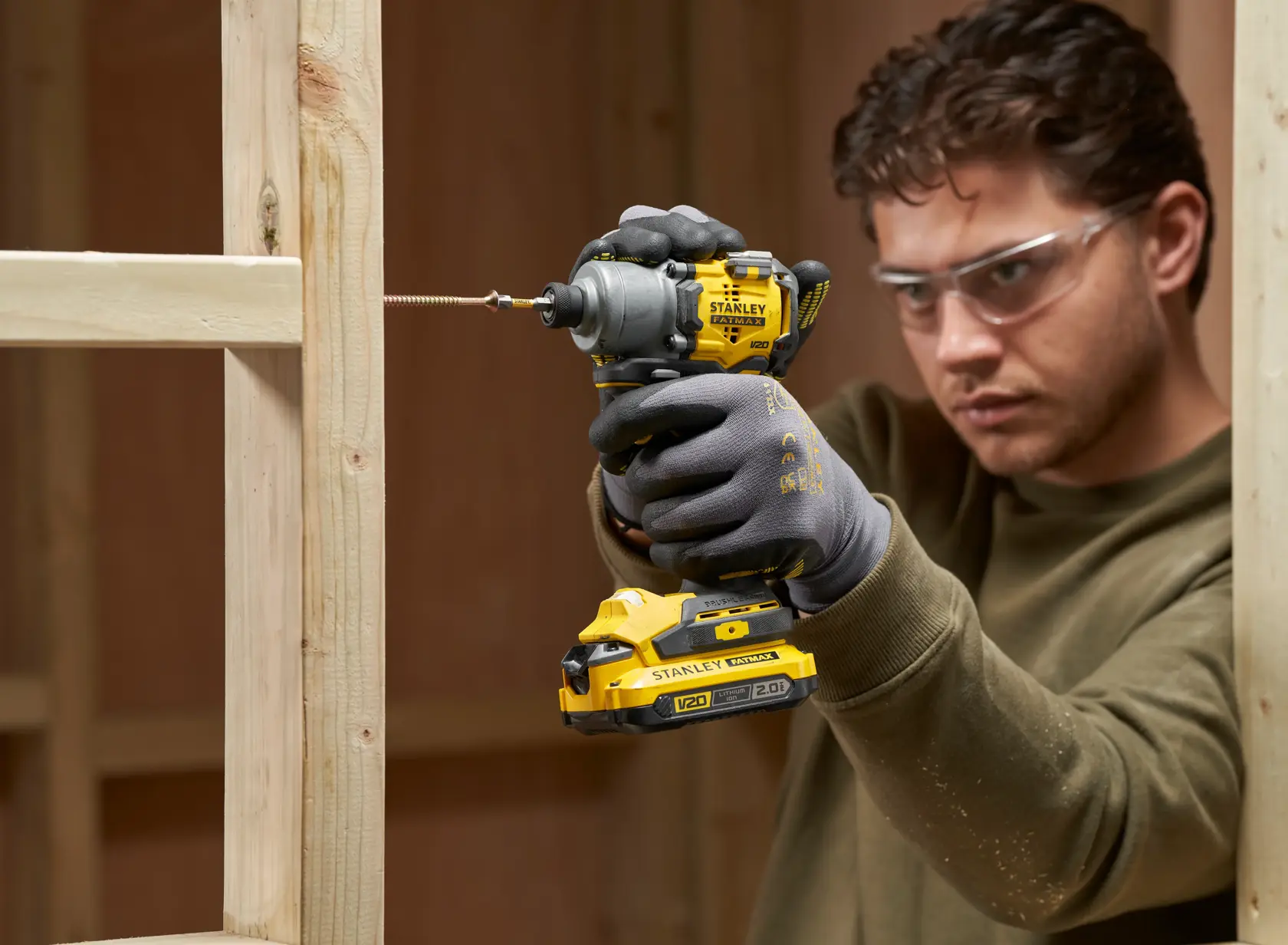 Foto dell’avvitatore ad impulsi STANLEY SFMCF830B in uso, avvitando su telaio in legno, utente con guanti.