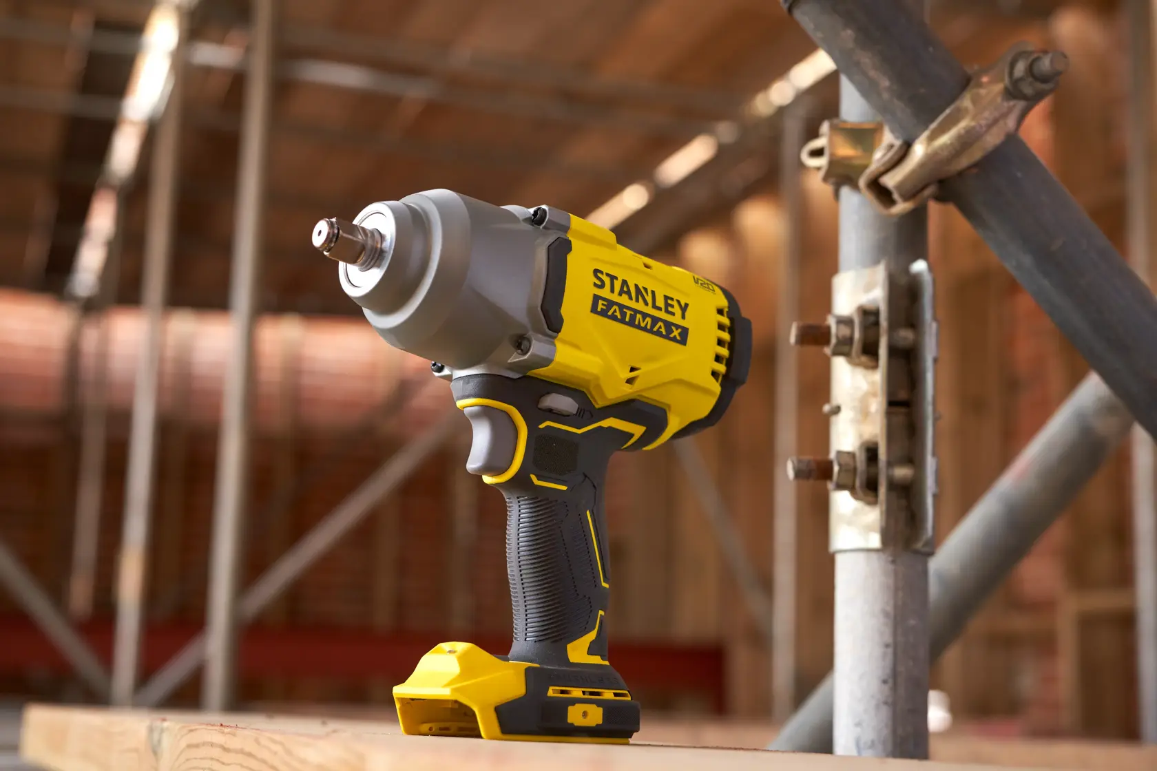 Avvitatore a impulsi cordless STANLEY SFMCF940B, giallo e nero, posizionato su superficie di legno in cantiere.