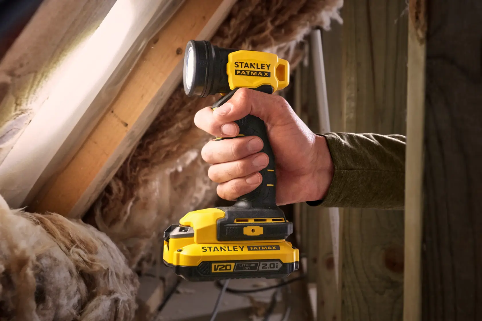Foto della lampada da lavoro gialla e nera a batteria STANLEY SFMCL020B tenuta in mano in una soffitta.