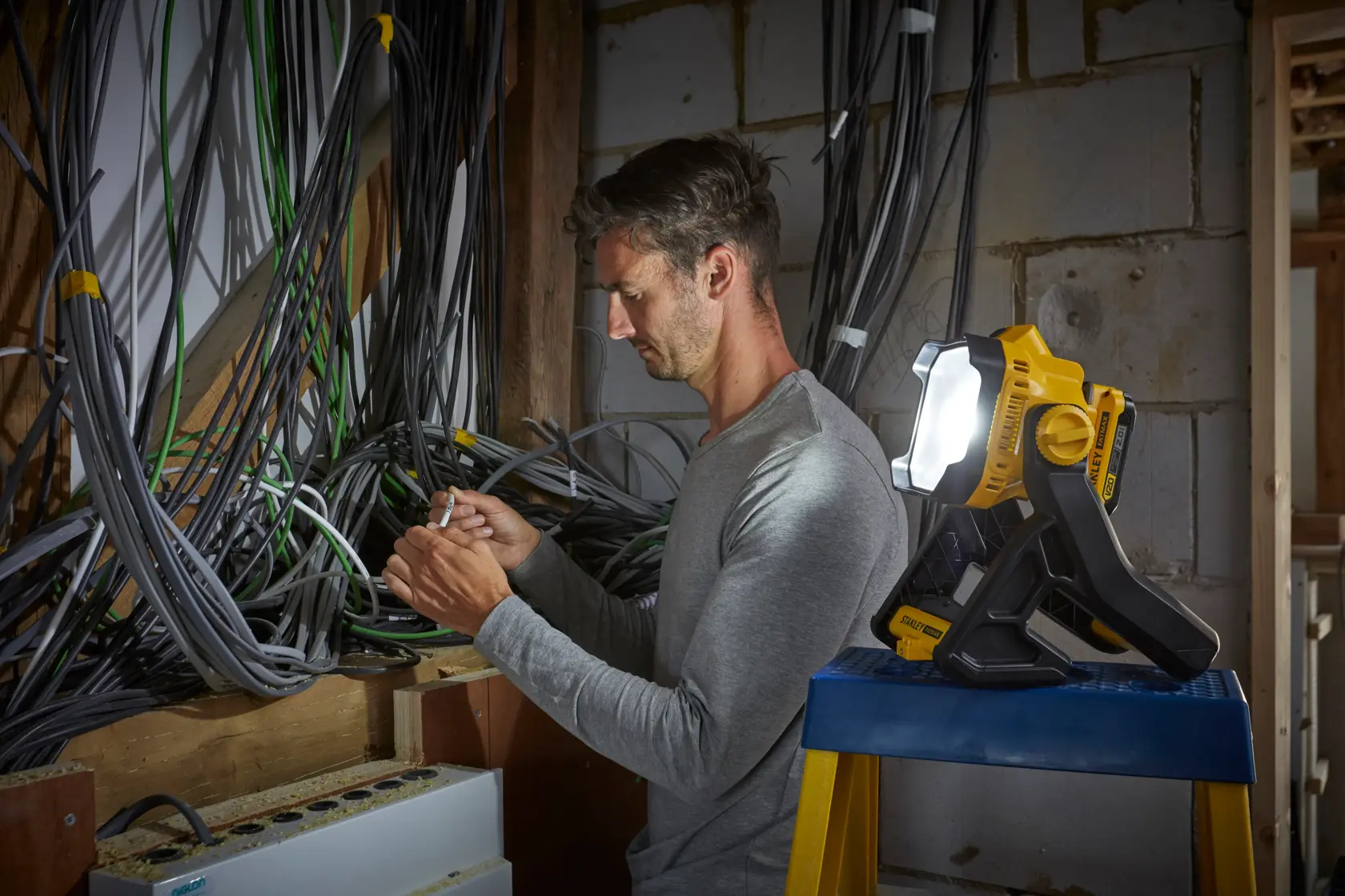 Stanley SFMCL030B luce da lavoro illumina elettricista che lavora tra cavi su parete non finita.