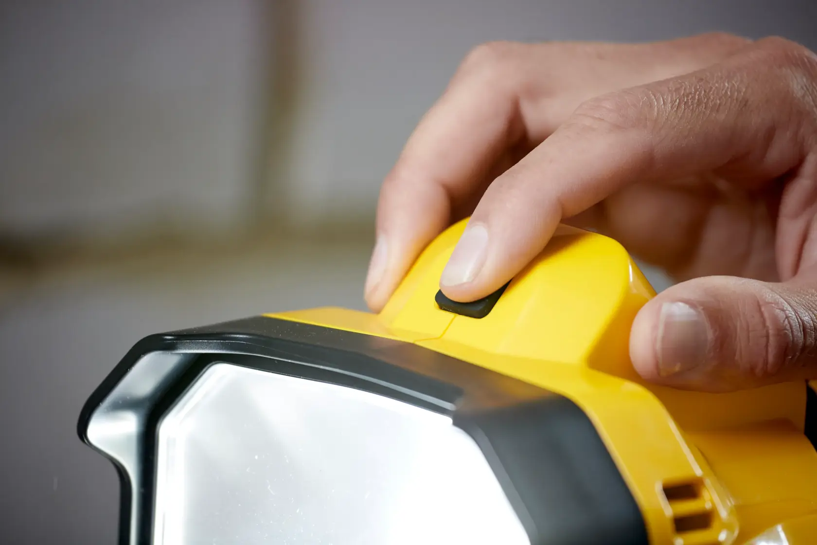 STANLEY SFMCL030B luce da lavoro LED in primo piano, dito sul pulsante, corpo giallo e nero.