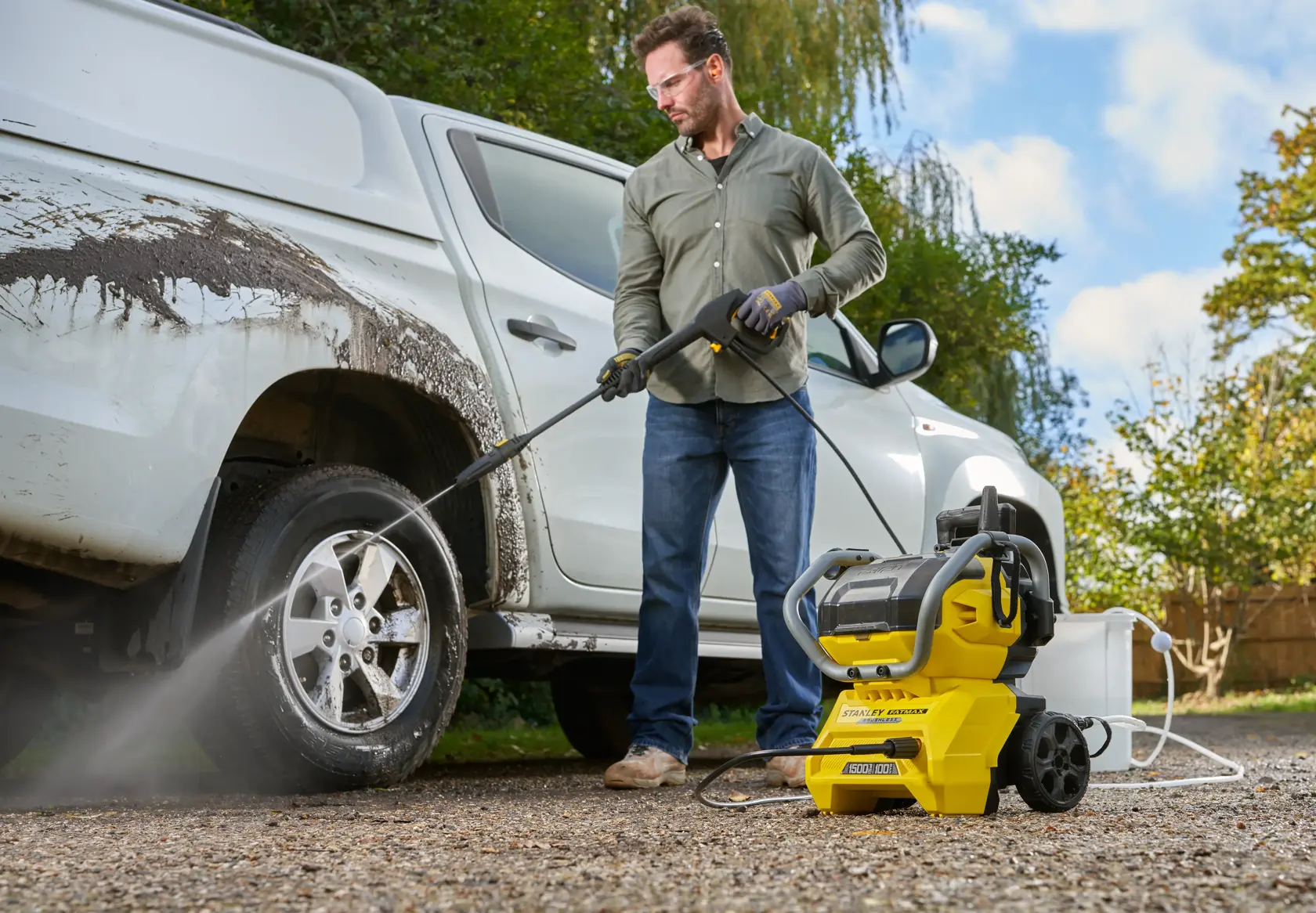 Idropulitrice STANLEY SFMCPW1500B utilizzata all’aperto per pulire un camion infangato, con tubo collegato e getto d’acqua.
