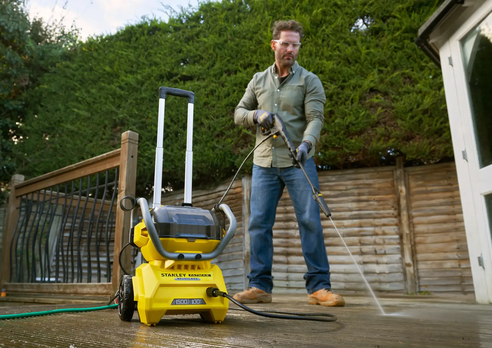 STANLEY SFMCPW1500B idropulitrice su patio, utilizzata da una persona per pulire un ponte in legno all’aperto.