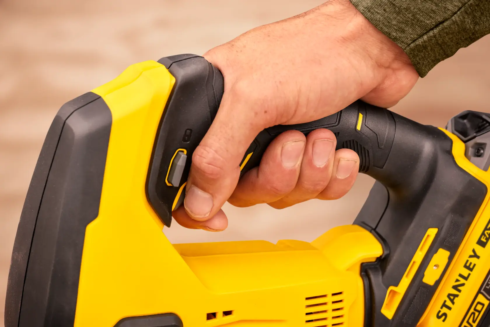 Foto di una mano che impugna la maniglia della sega a batteria STANLEY SFMCS600B, primo piano su utensile nero e giallo.