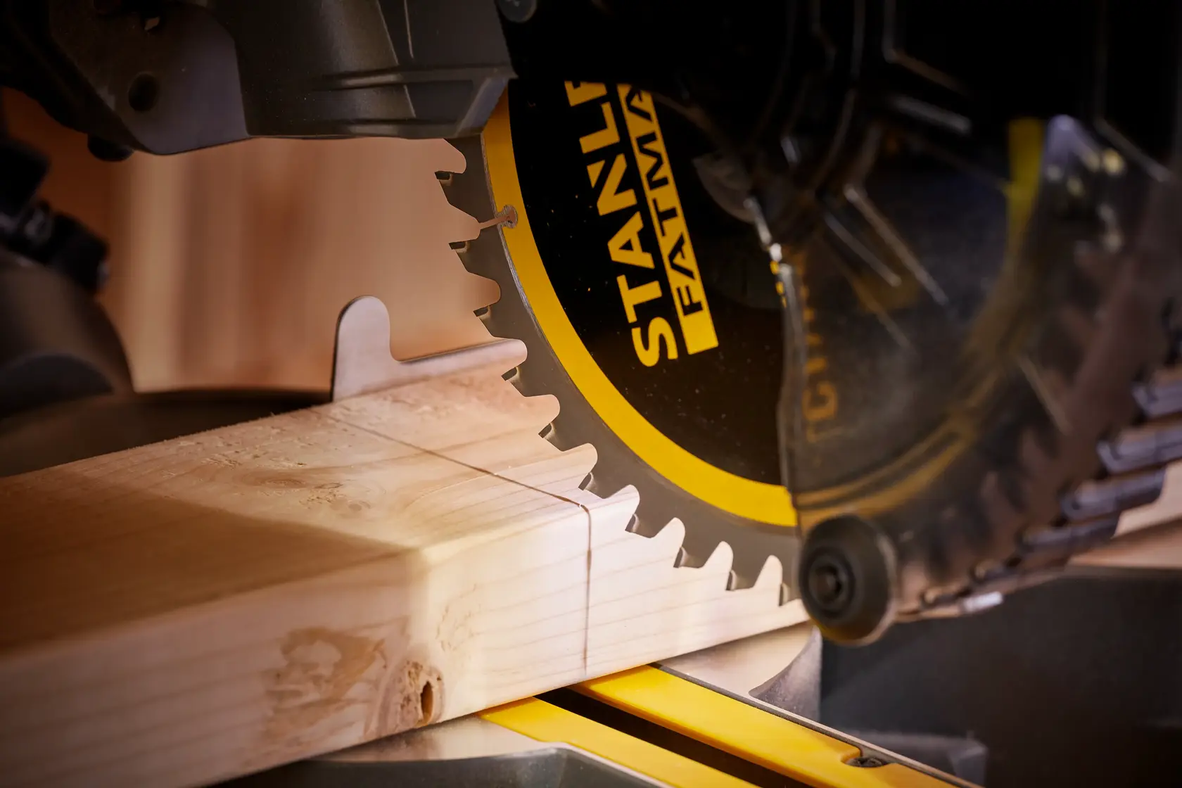 Dettaglio sega troncatrice STANLEY SFMCS701M1 che taglia legno, lama nera e gialla, contesto falegnameria.