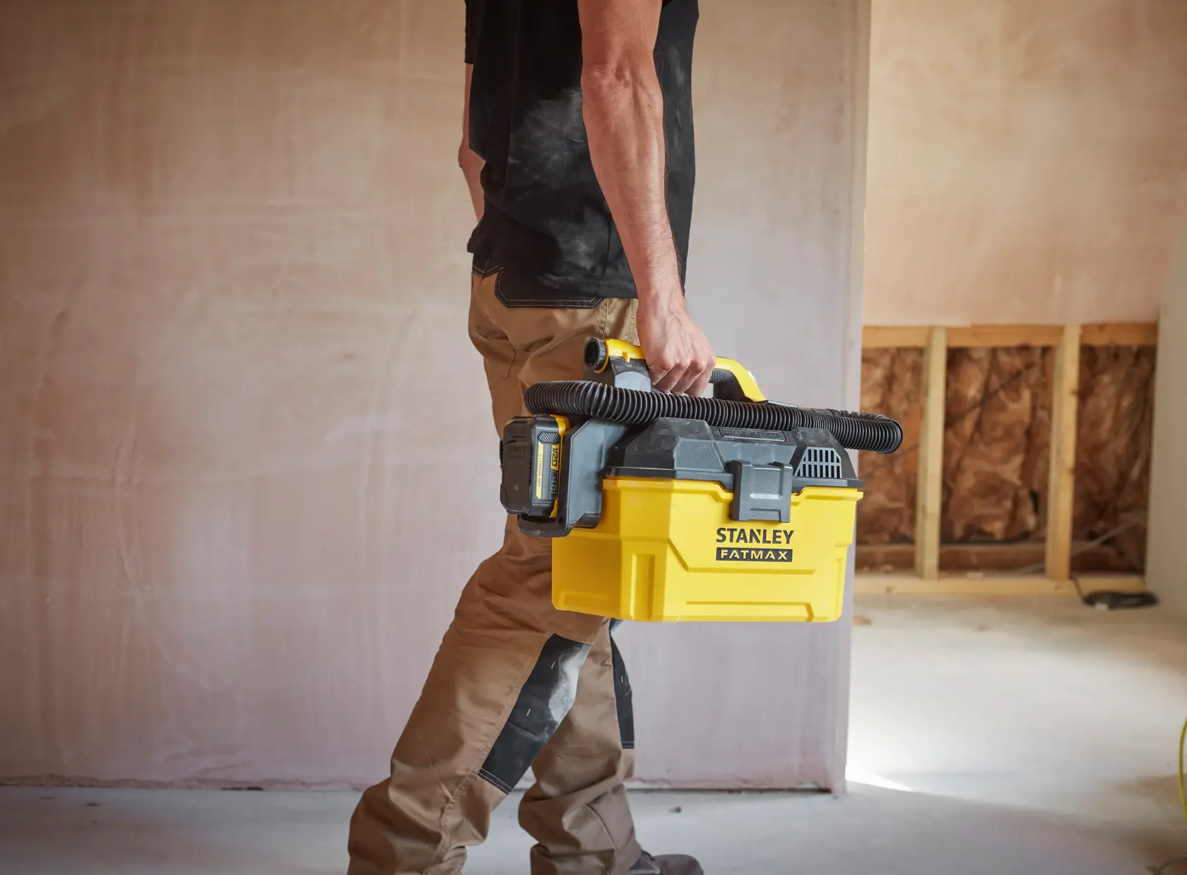 Persona che trasporta aspirapolvere portatile giallo STANLEY SFMCV002B con tubo nero in un cantiere.