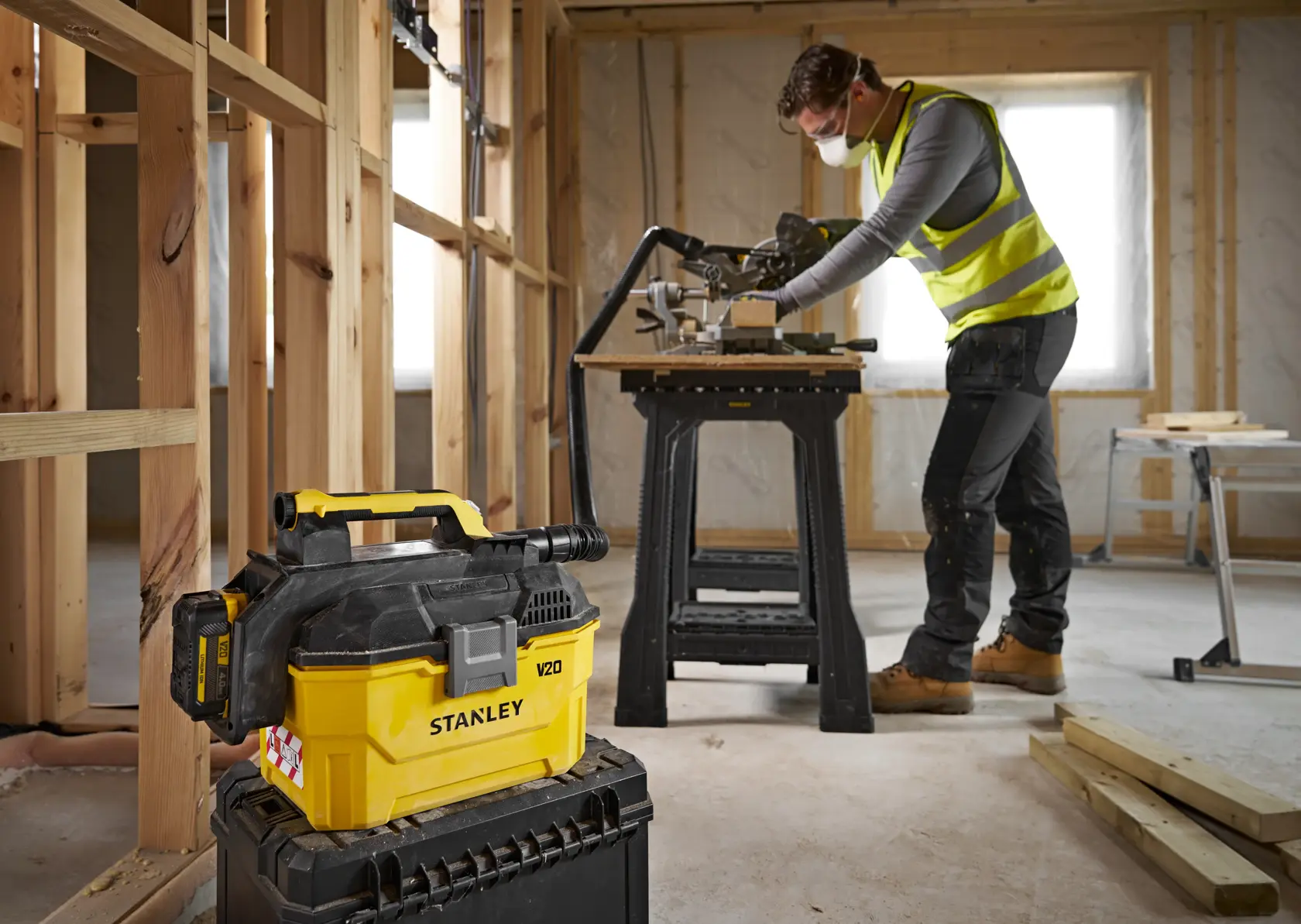 Aspirapolvere Stanley V20 su toolbox, operaio con gilet lavora in stanza non finita.