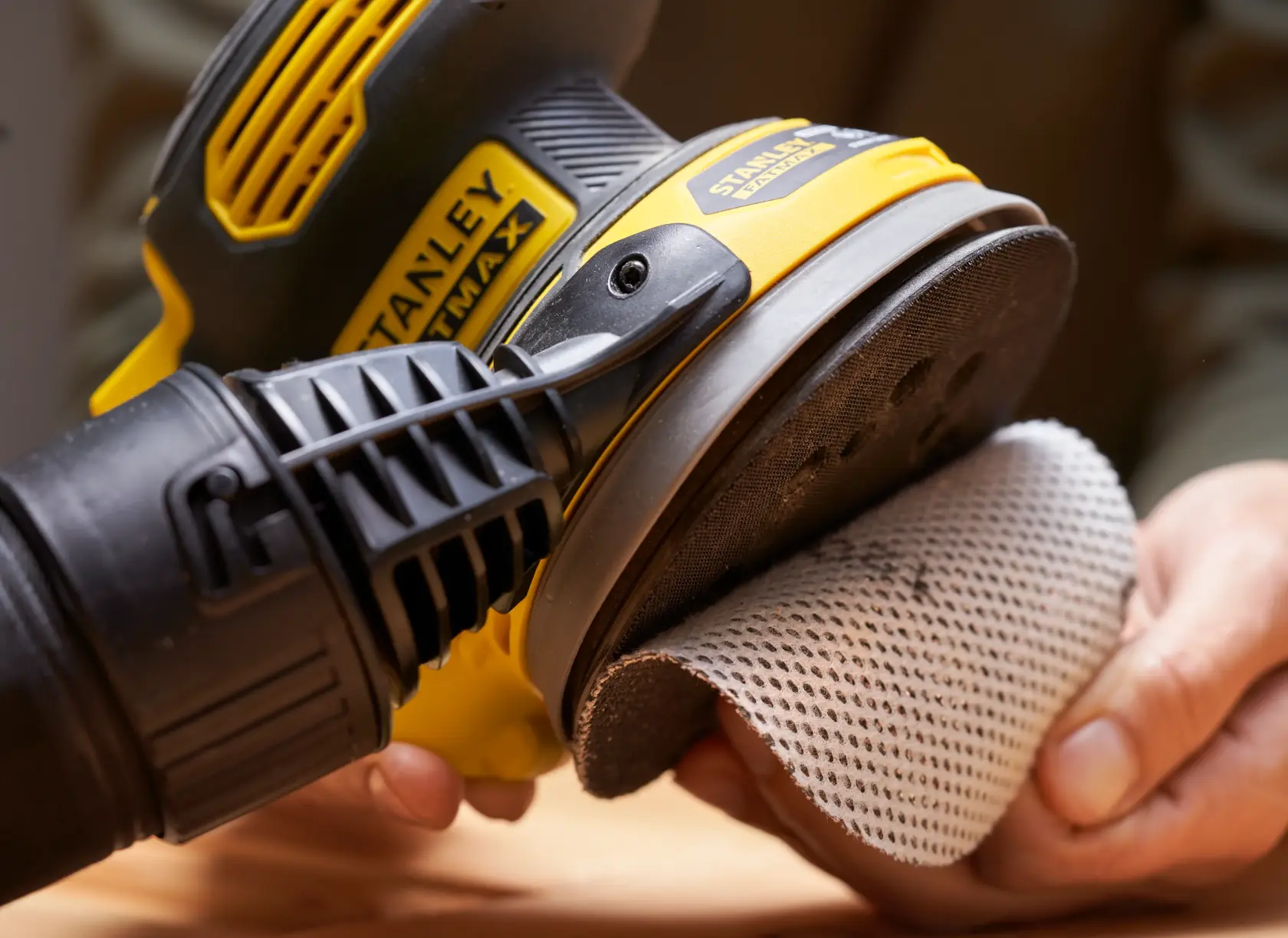 STANLEY SFMCW220B levigatrice tenuta in mano, pad abrasivo a rete in fase di applicazione, vista ravvicinata.