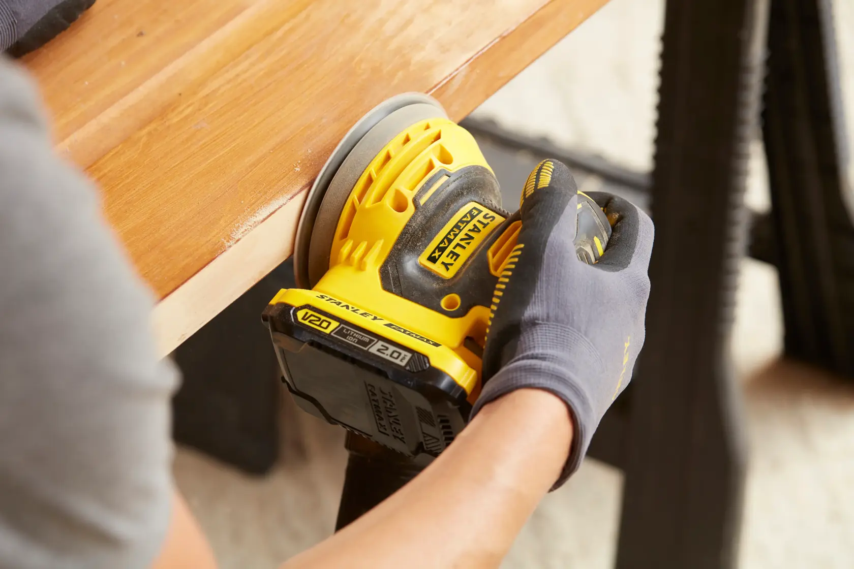 Foto della levigatrice cordless STANLEY SFMCW220B in uso su superficie di legno, angolo ravvicinato.