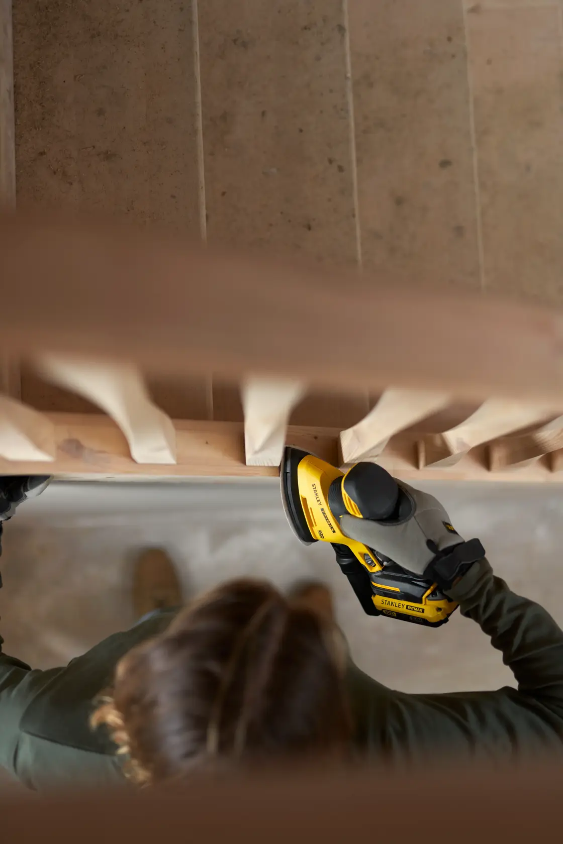 Foto della levigatrice STANLEY SFMCW221D1S utilizzata su una ringhiera di scala in legno dall’alto.