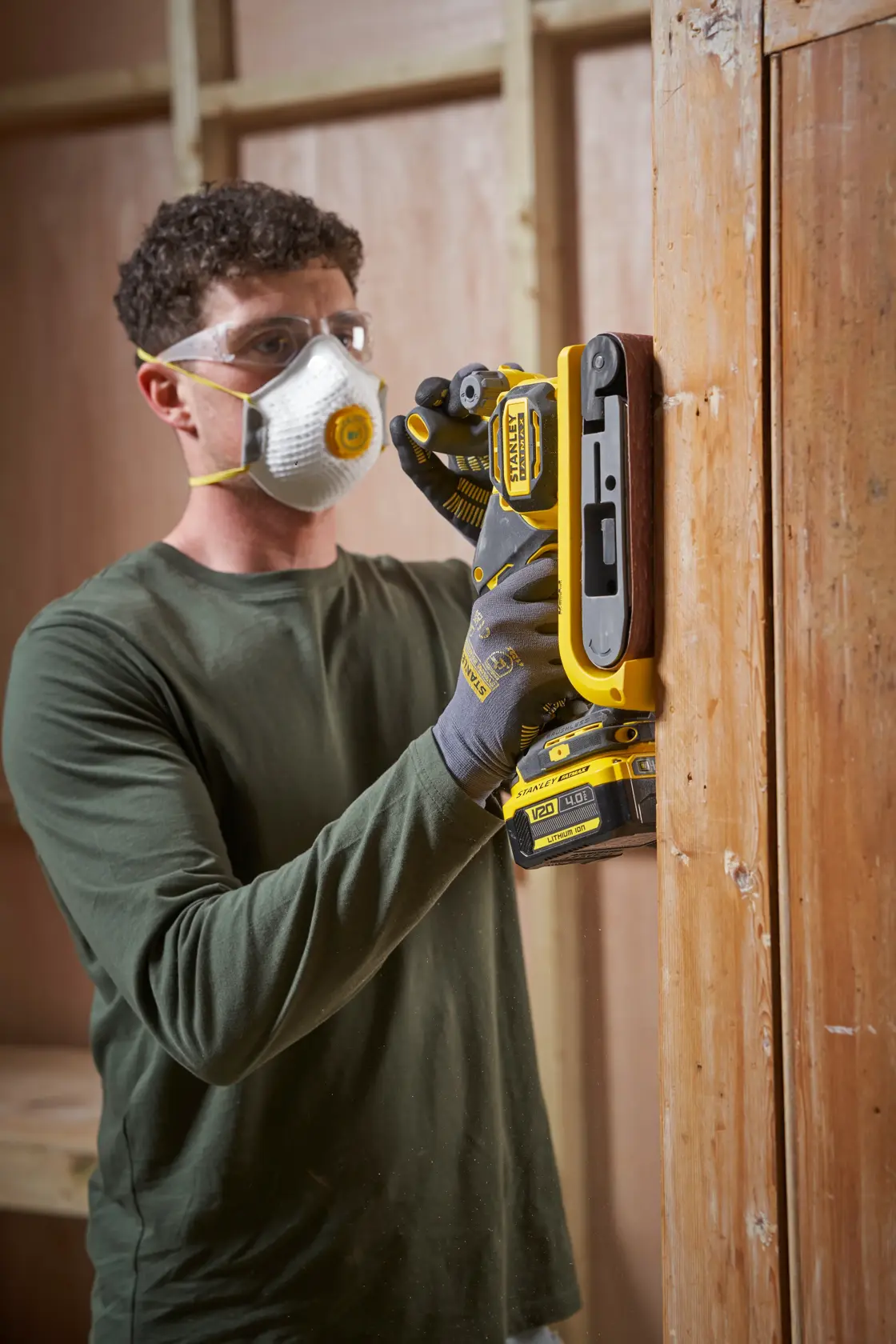 STANLEY SFMCW223B-XJ levigatrice a nastro usata su porta in legno, utensile giallo e nero, ambiente laboratorio.
