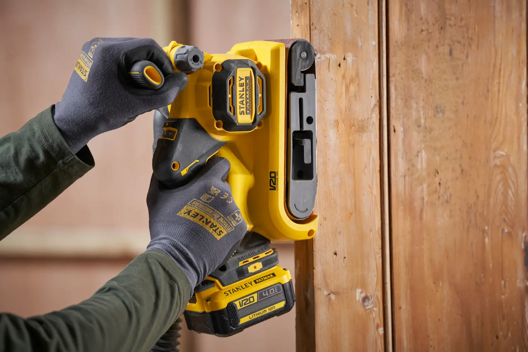 STANLEY SFMCW223B-XJ levigatrice senza fili in uso sul legno, primo piano dello strumento giallo tenuto da mani con guanti.